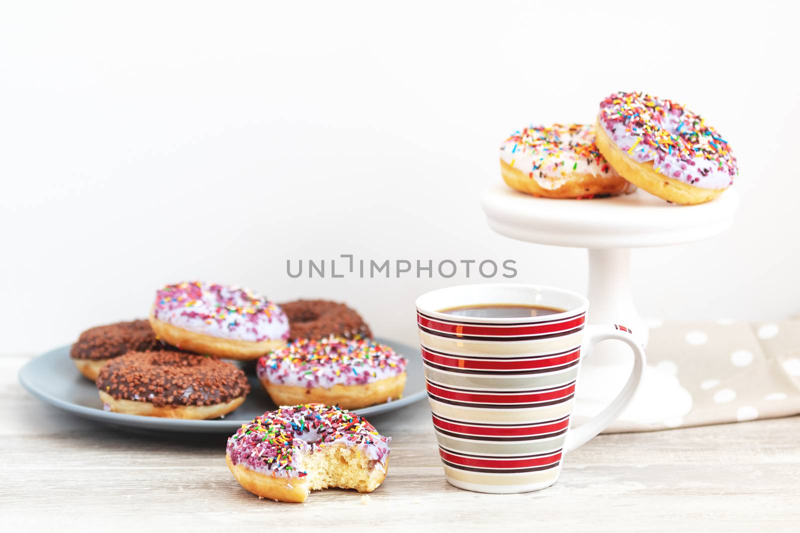 Delicious glazed donuts and cup of coffee on light wooden background. Beautiful romantic breakfast or lunch concept. Shallow depth of the field.