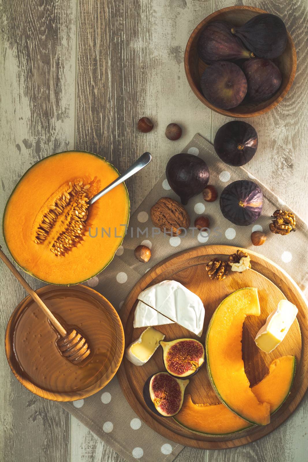 Cantaloupe melon sliced with Camembert, basil leaves, fig, nuts, honey and dried cherry. Italian appetizer on wooden background.