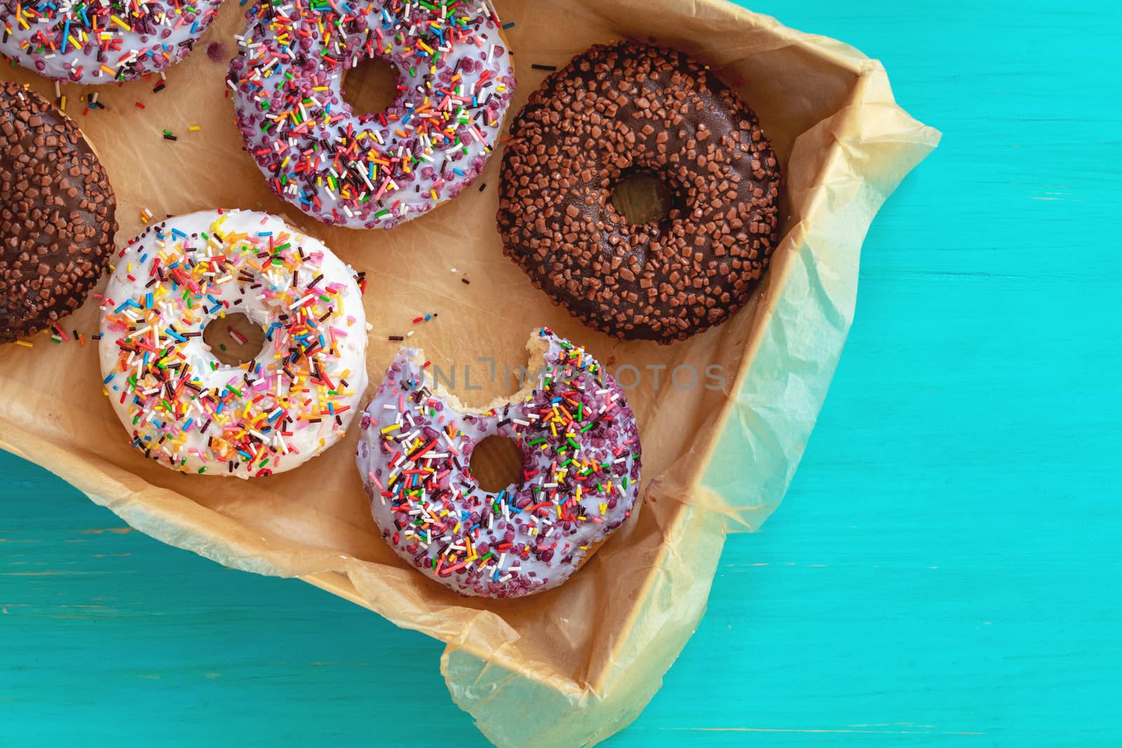 Delicious glazed donuts in box on turquoise blue surface. Flat lay minimalist food art background. Top view.