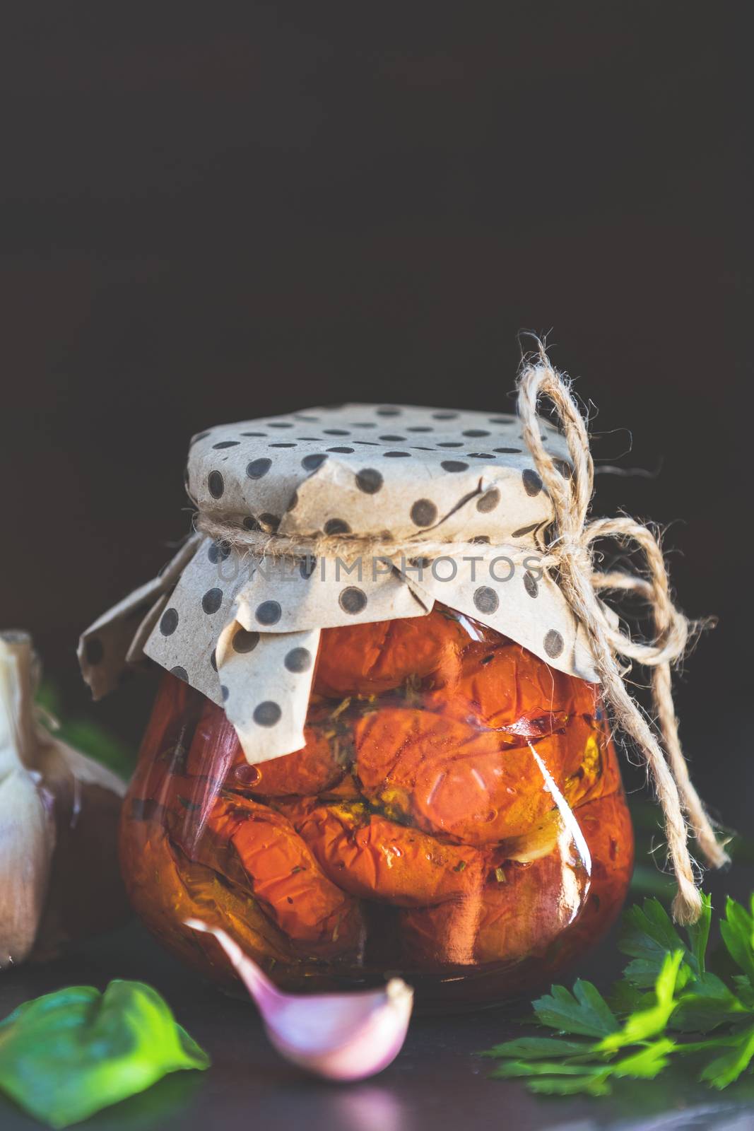 Sun dried tomatoes in glass jar, onion, basil leaves and garlic on cutting board, on wooden background