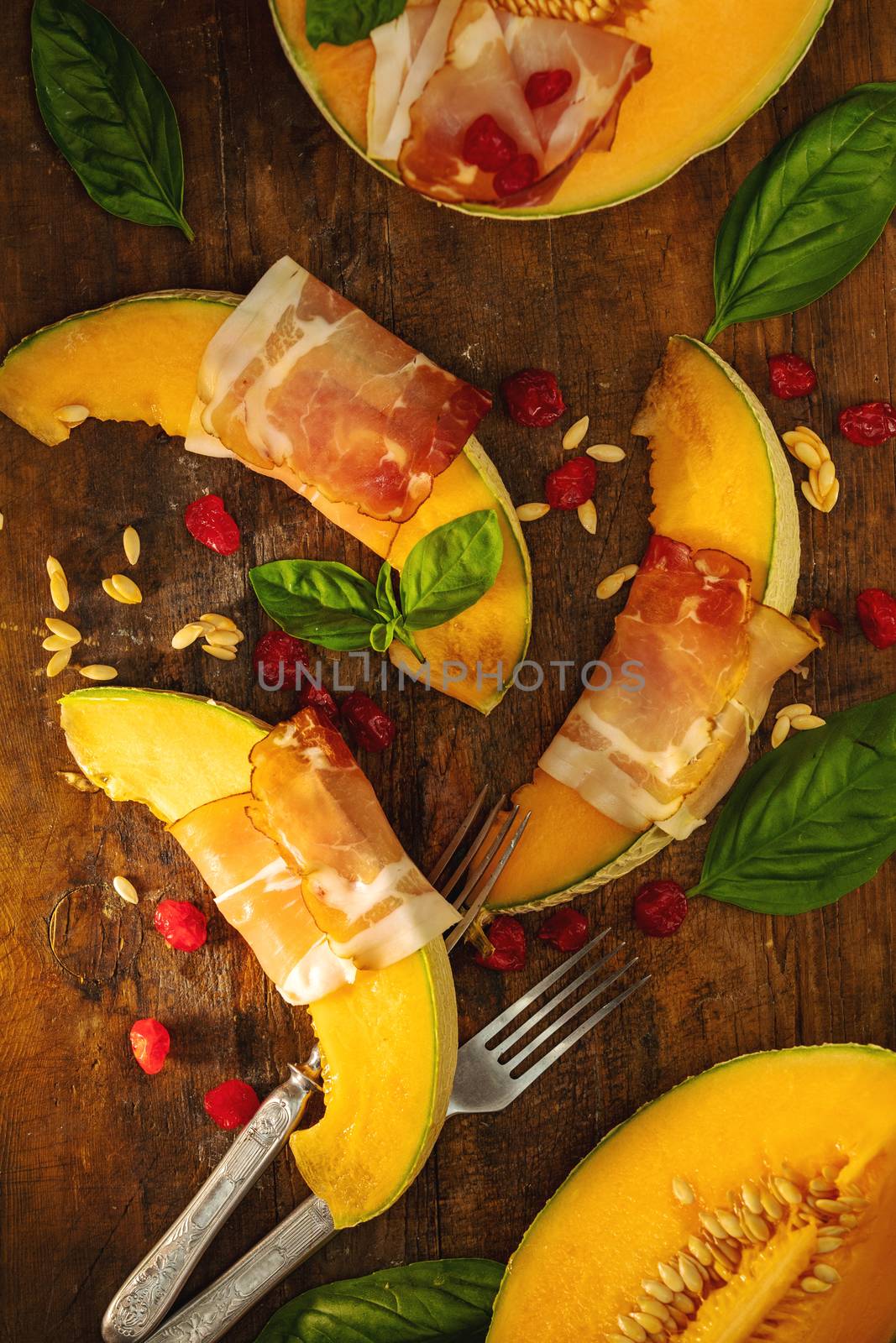 Cantaloupe melon sliced with Prosciutto jamon, basil leaves, fig and dried cherry. Italian appetizer on wooden background.