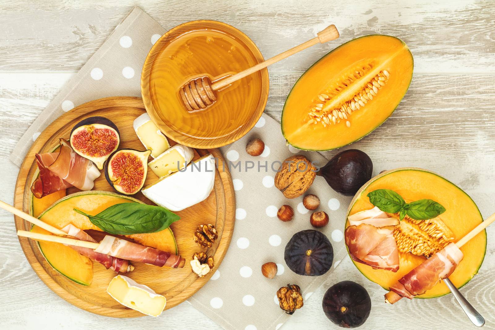 Cantaloupe melon sliced with Prosciutto jamon, basil leaves, fig, Camembert, honey and dried cherry. Italian appetizer on wooden background.