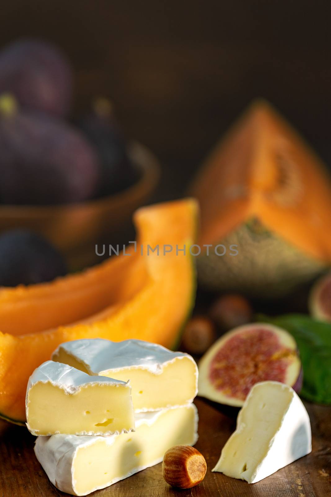 Cantaloupe melon sliced with Camembert, basil leaves, fig, and dried cherry. Italian appetizer on wooden background.