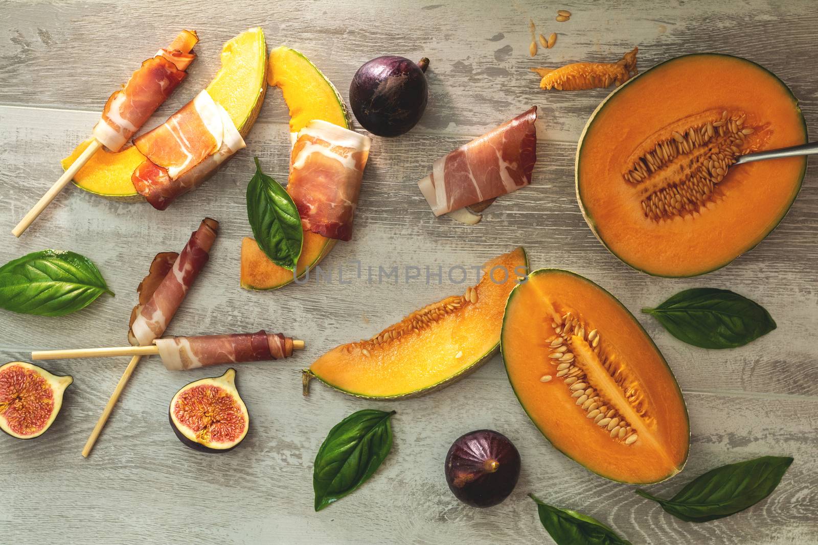 Cantaloupe melon sliced with Prosciutto jamon, basil leaves, fig and dried cherry. Italian appetizer on wooden background.