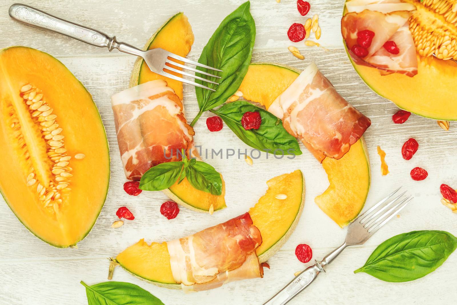 Cantaloupe melon sliced with Prosciutto jamon, basil leaves, fig and dried cherry. Italian appetizer on wooden background