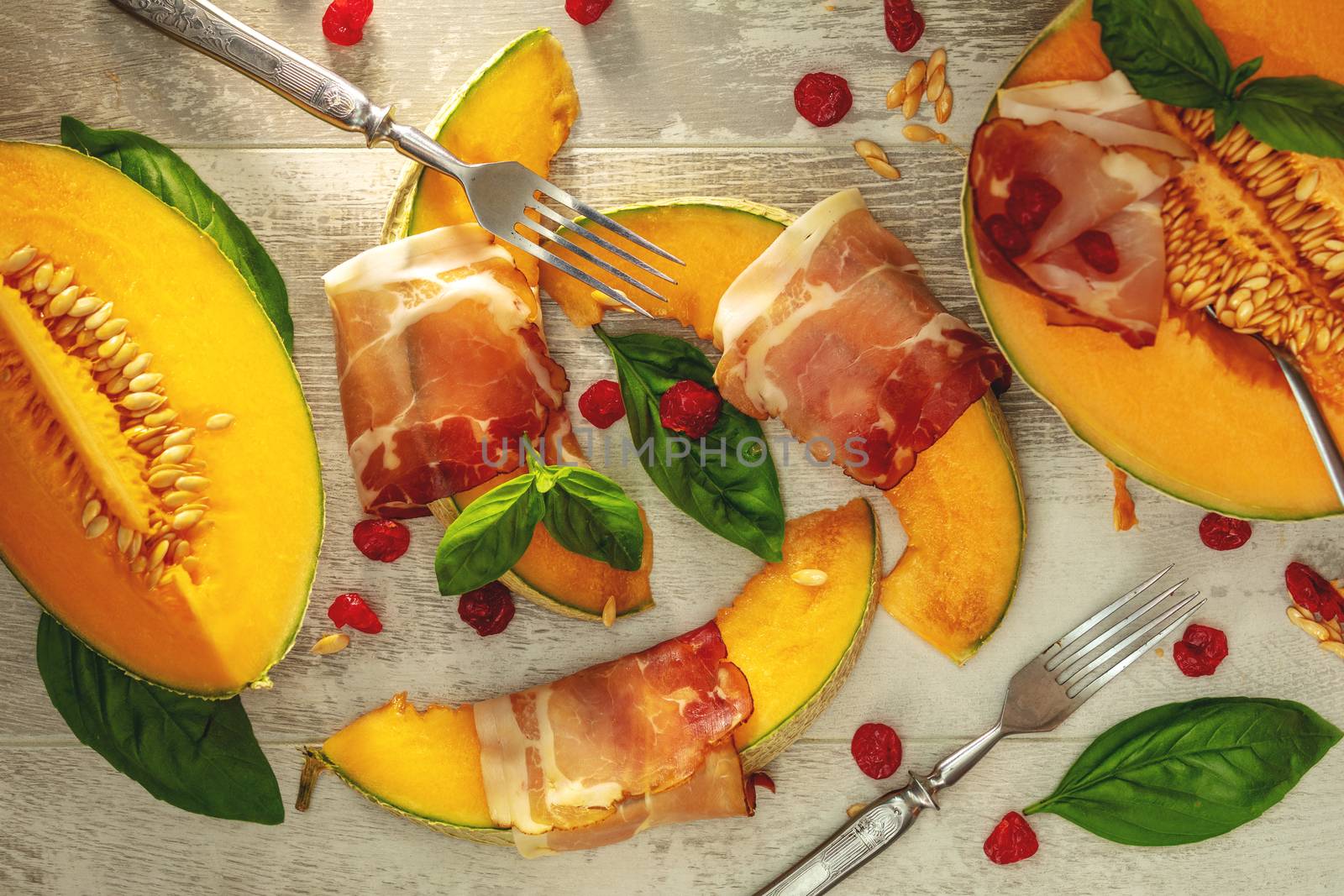 Cantaloupe melon sliced with Prosciutto jamon, basil leaves, fig and dried cherry. Italian appetizer on wooden background.