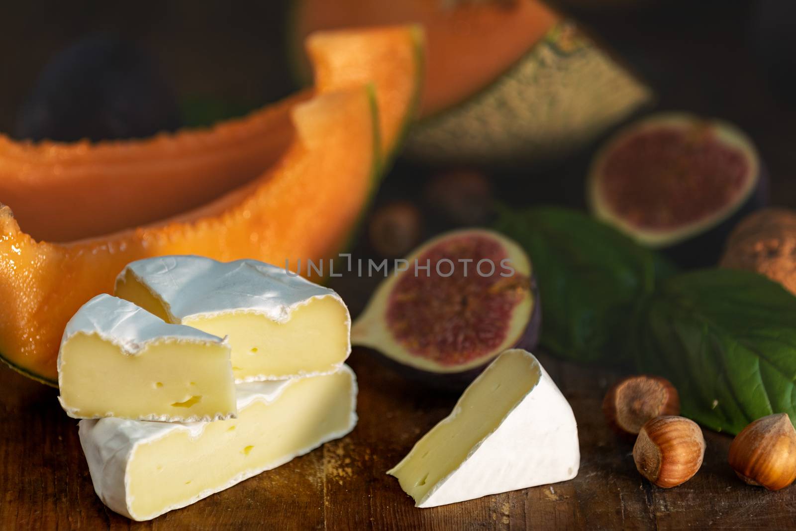 Cantaloupe melon sliced with Camembert, basil leaves, fig, and dried cherry. Italian appetizer on wooden background.