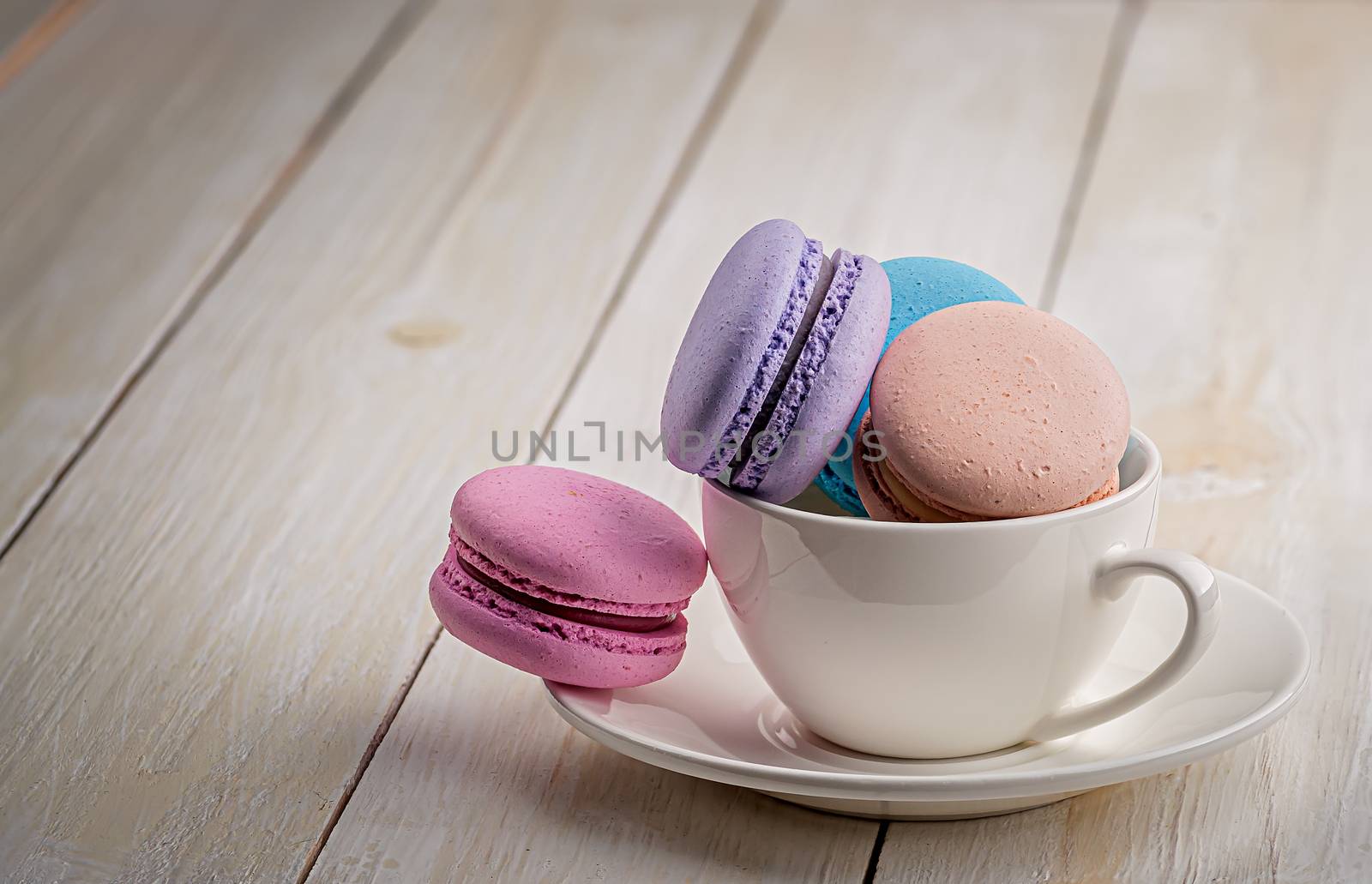 Multicolored macaroons in white cup on wooden table
