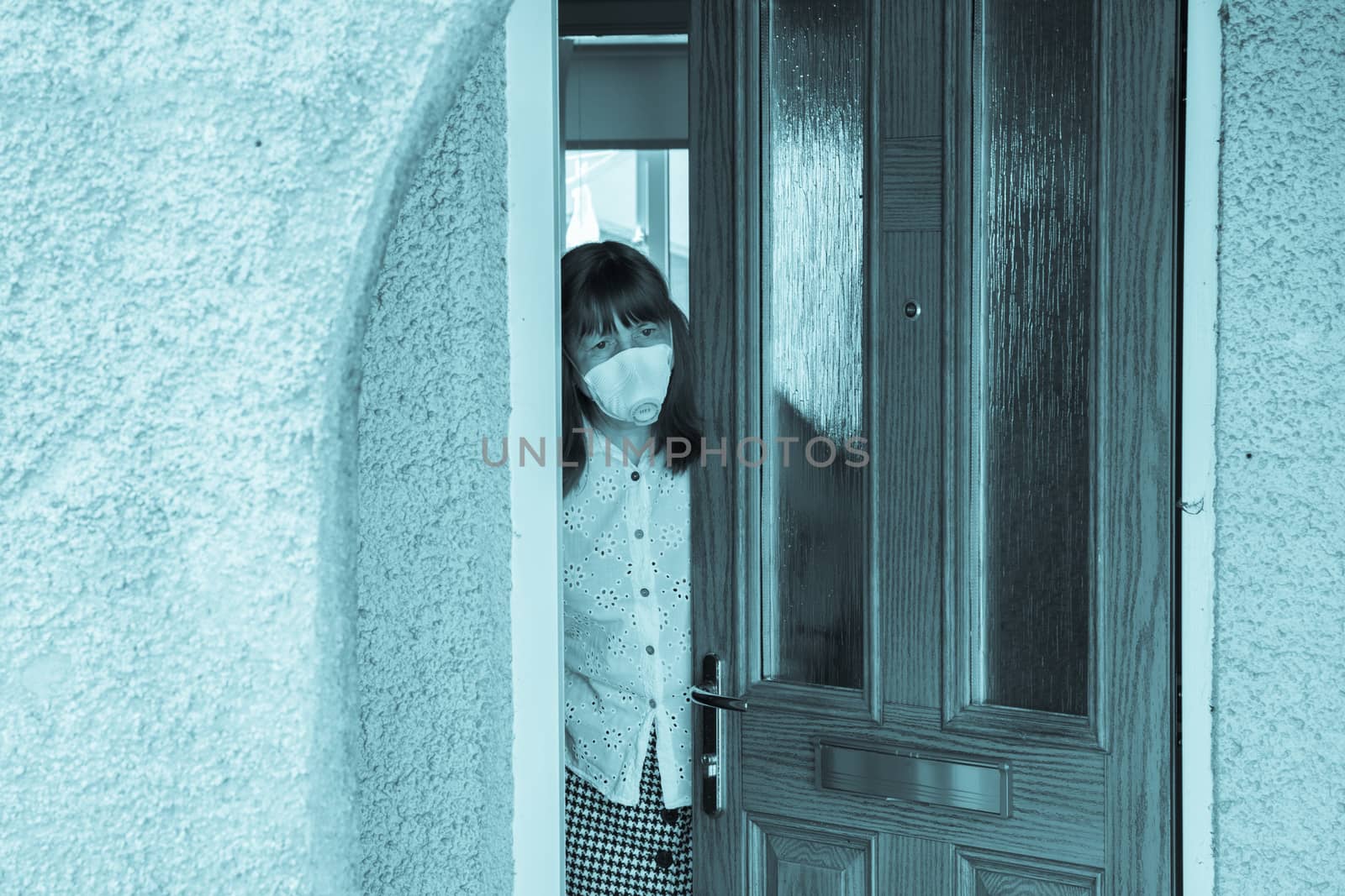 woman in a protective medical mask looking out from behind a partially open door. Coronavirus epidemic UK