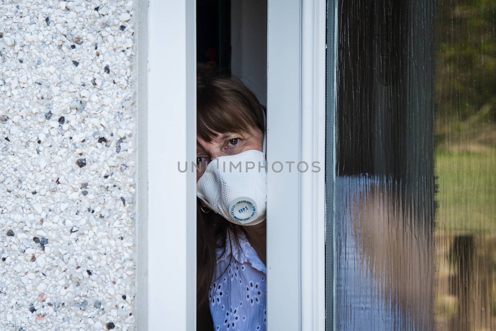 woman in a protective medical mask looking out from behind a partially open door. Coronavirus epidemic UK