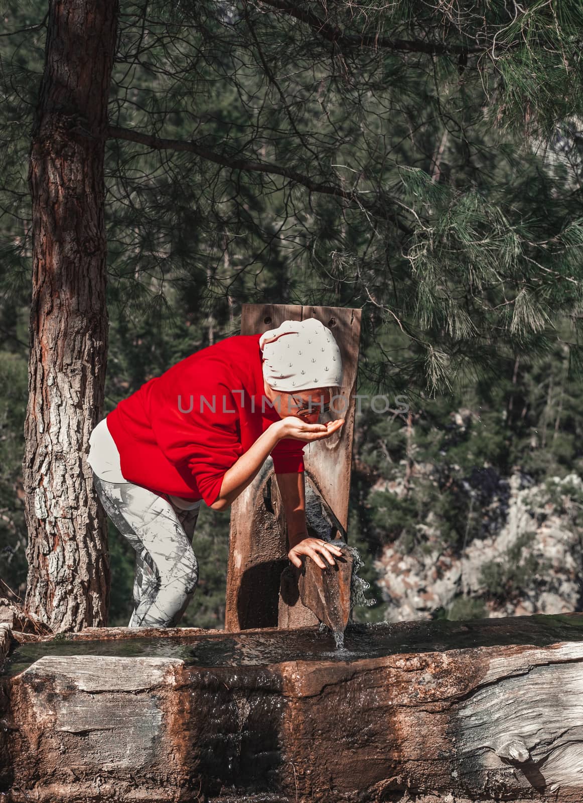 Adult woman drinking cold water from the spring out in the nature.