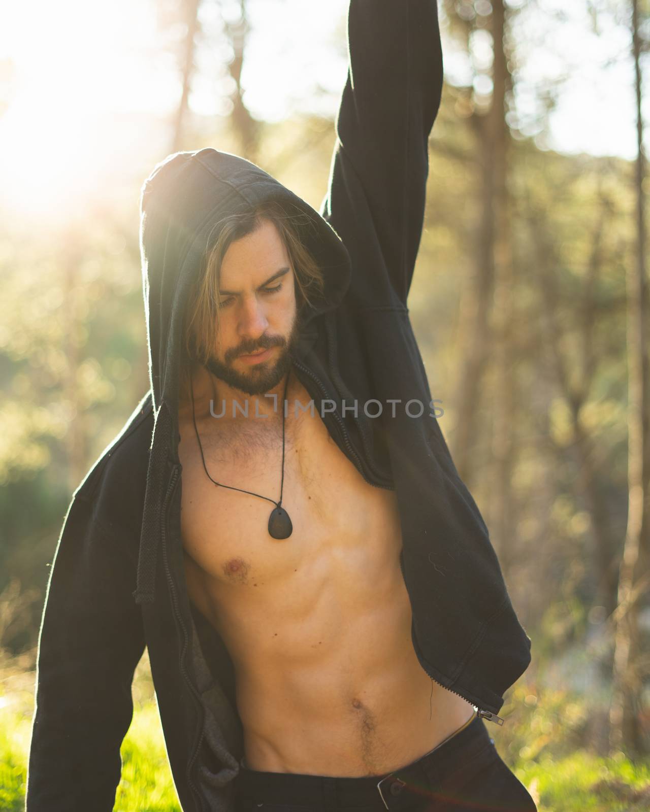 Young bearded man doing pull ups in the park with beautiful sunset on the mountain