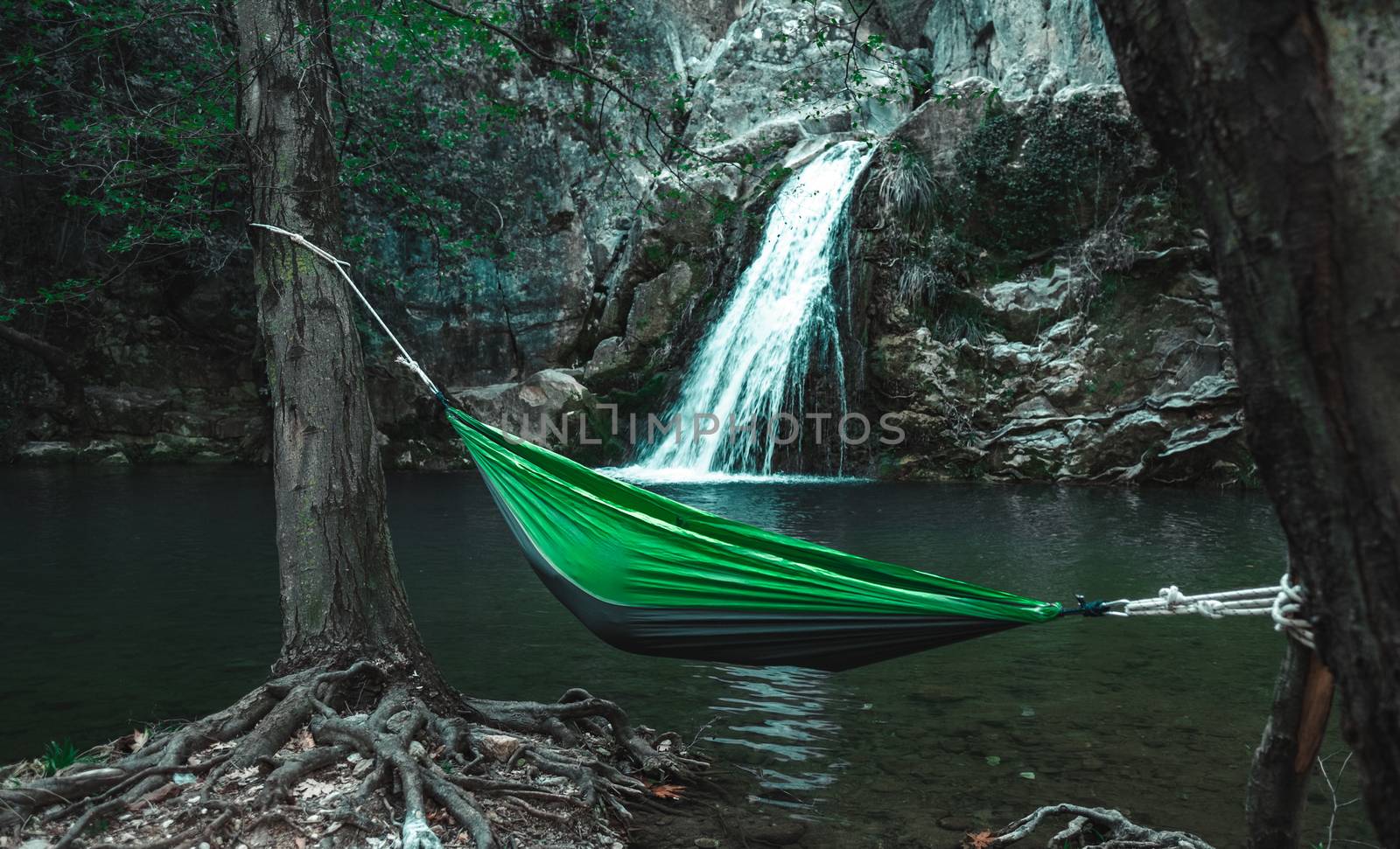 Green hammock with person in it between trees in front of a waterfall in Eksili, Antalya, Turkey.