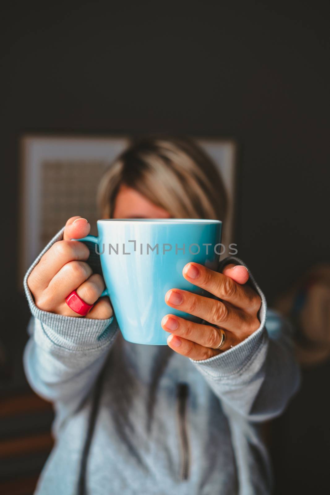 Woman holding a blue cup in front of her face at cozy ambience.
