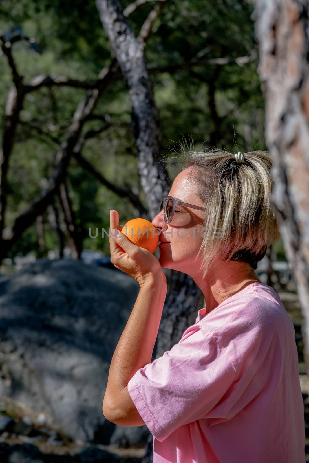 Adult woman holding orange in the palm and smelling it in the nature. by Emurado