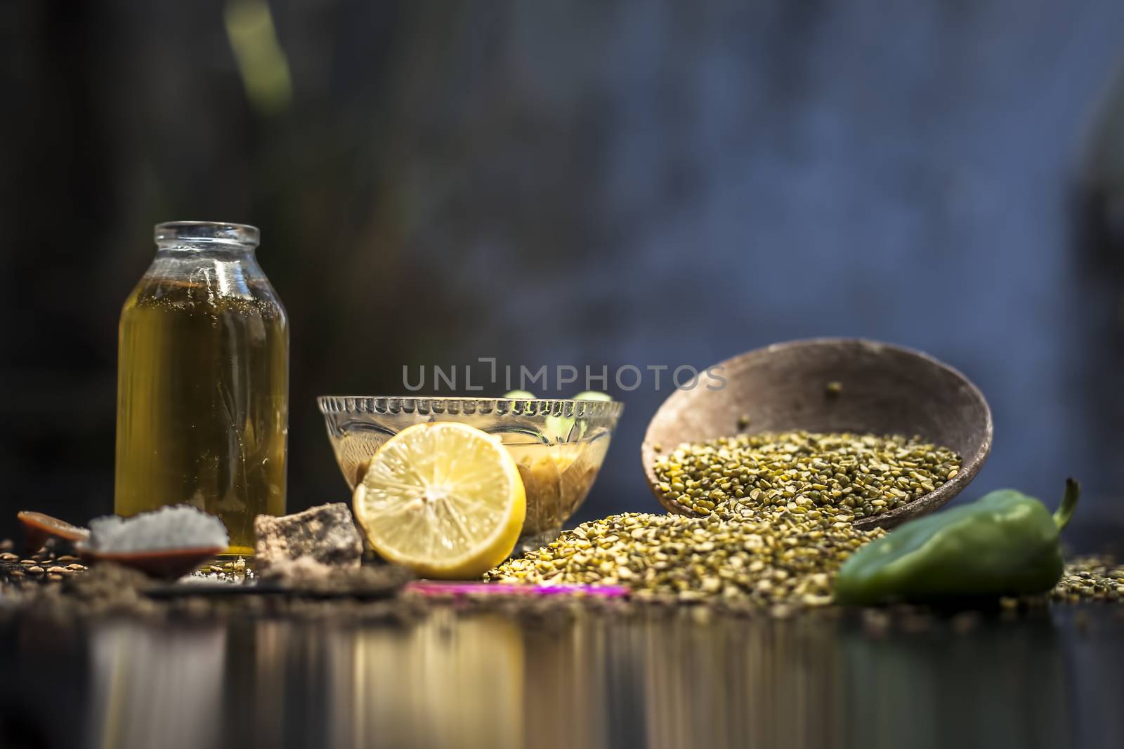 Close up of mung dal soup in glass bowl along with entire constituents with it which are mung bean,green gram, asafoetida, cumin, green chili, black peppercorns, lemon juice and salt on black surface. by mirzamlk