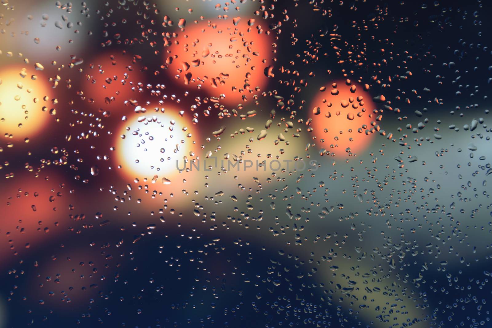 Raindrops on a car window with beautifully blurred background of street traffic lights