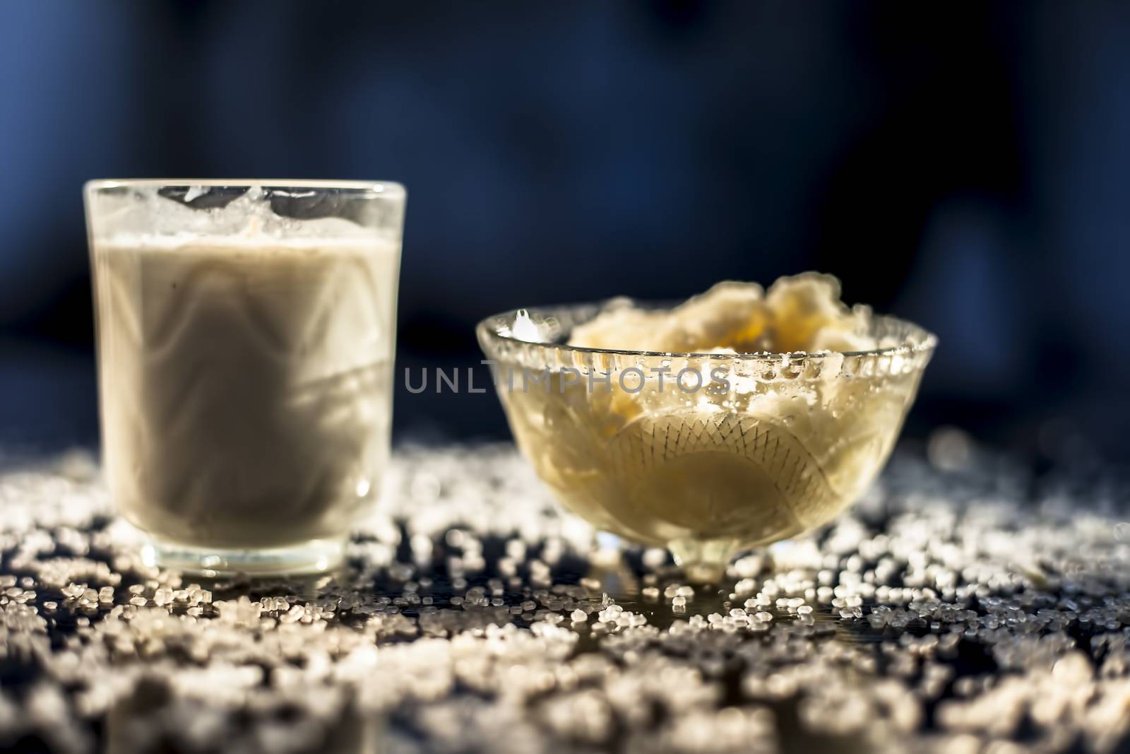 Close up of glass bowl of pure milk well mixed with hot milk in it on black wooden glossy surface along with raw ghee clarified butter and some sugar crystals spread on the surface. Horizontal shot.