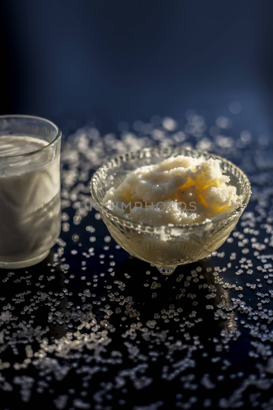 Close up of glass bowl of pure milk well mixed with hot milk in it on black wooden glossy surface along with raw ghee clarified butter and some sugar crystals spread on the surface. Vertical shot. by mirzamlk