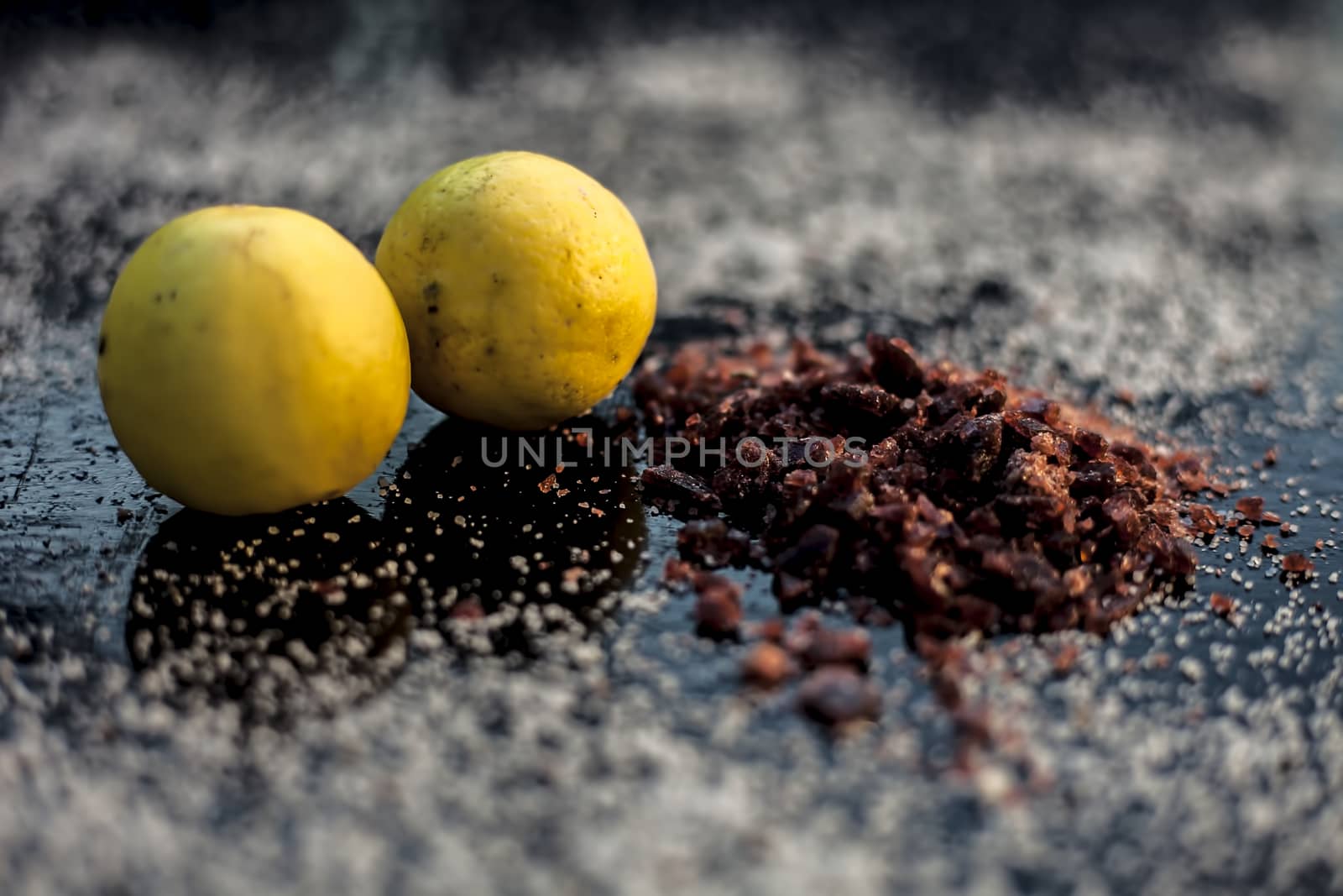 Pair of raw organic ripe yellow lemons on a black surface along with some rock salt (sendha namak) and white or common salt spread on the surface. Used for the salt remedy of skin and as a face mask.