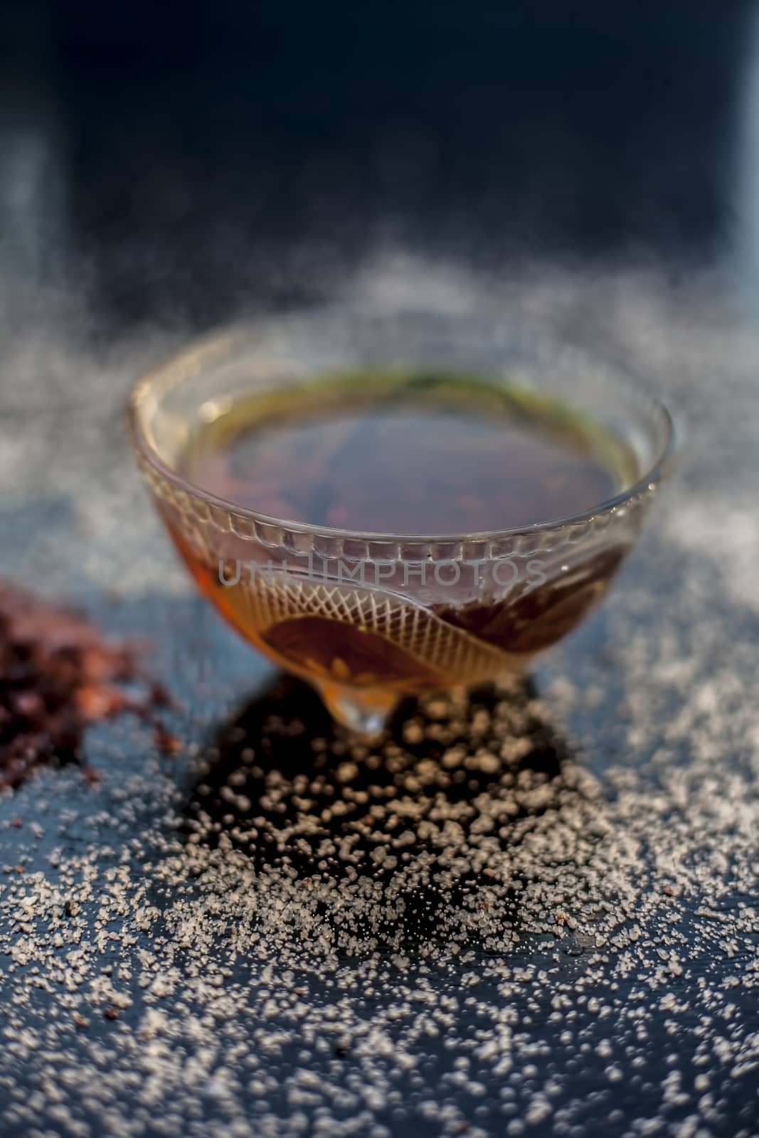 Close up of a glass bowl full of organic honey used in spa on black glossy surface with some white crystals spread on the surface. Vertical shot.