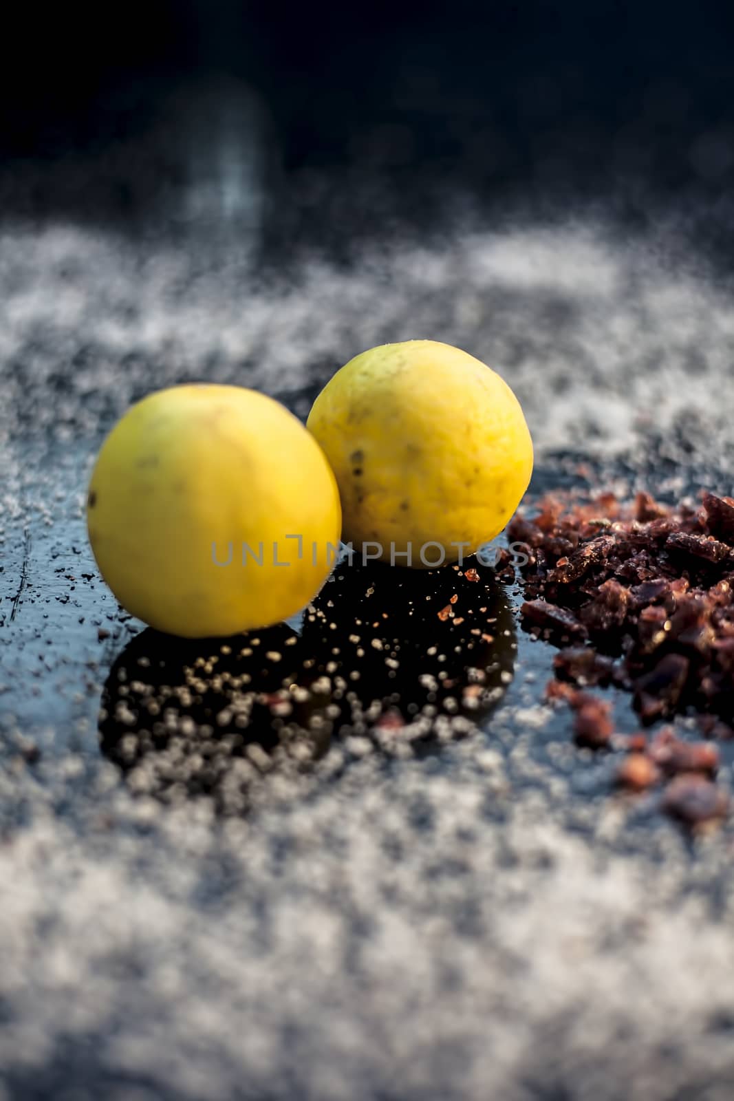 Pair of raw organic ripe yellow lemons on a black surface along with some rock salt (sendha namak) and white or common salt spread on the surface. Used for the salt remedy of skin and as a face mask. by mirzamlk