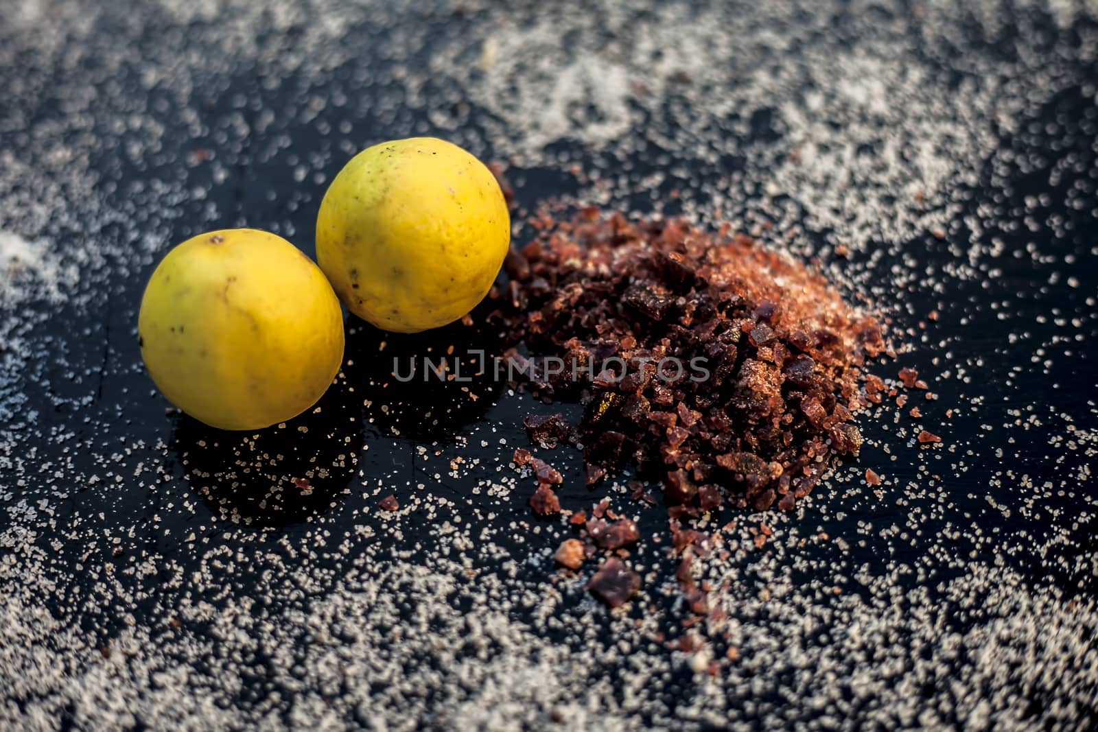 Pair of raw organic ripe yellow lemons on a black surface along with some rock salt (sendha namak) and white or common salt spread on the surface. Used for the salt remedy of skin and as a face mask.