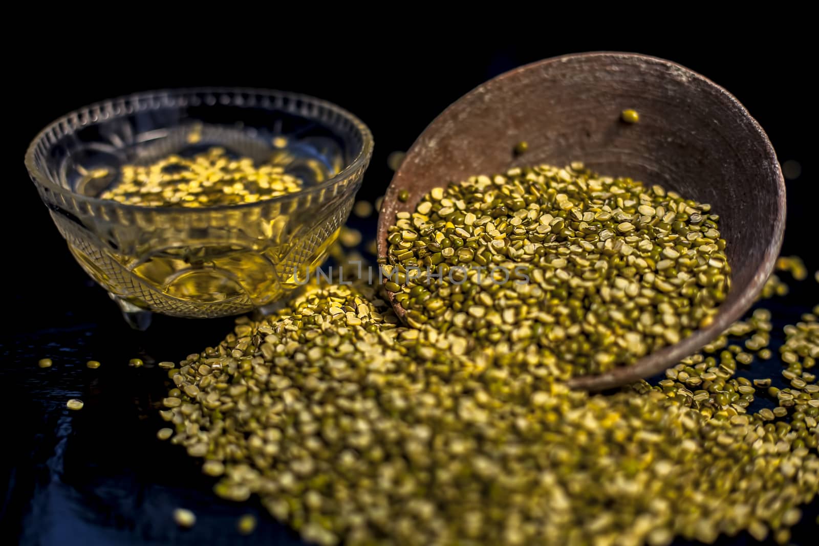 Close shot of mung bean or moong dal in a clay bowl along with some water and moong dal well mixed on a black glossy surface. Horizontal shot with Rembrandt lighting technique.