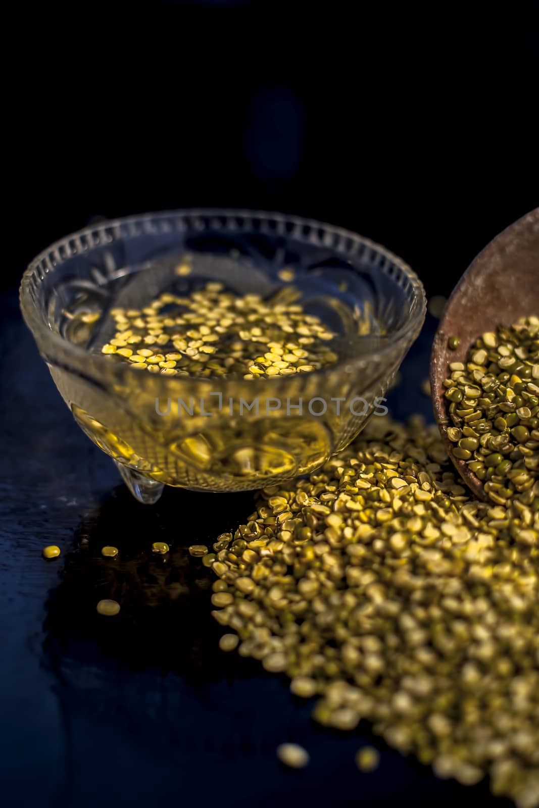 Close shot of mung bean or moong dal in a clay bowl along with some water and moong dal well mixed on a black glossy surface.Vertical shot with Rembrandt lighting technique.