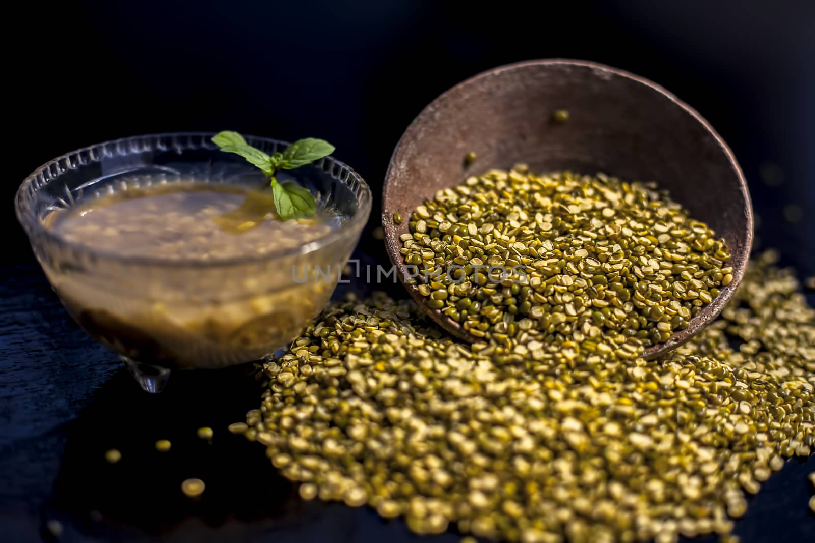 Close shot of mung bean or moong dal in a clay bowl along with some water and moong dal well mixed on a black glossy surface. Horizontal shot with Rembrandt lighting technique.