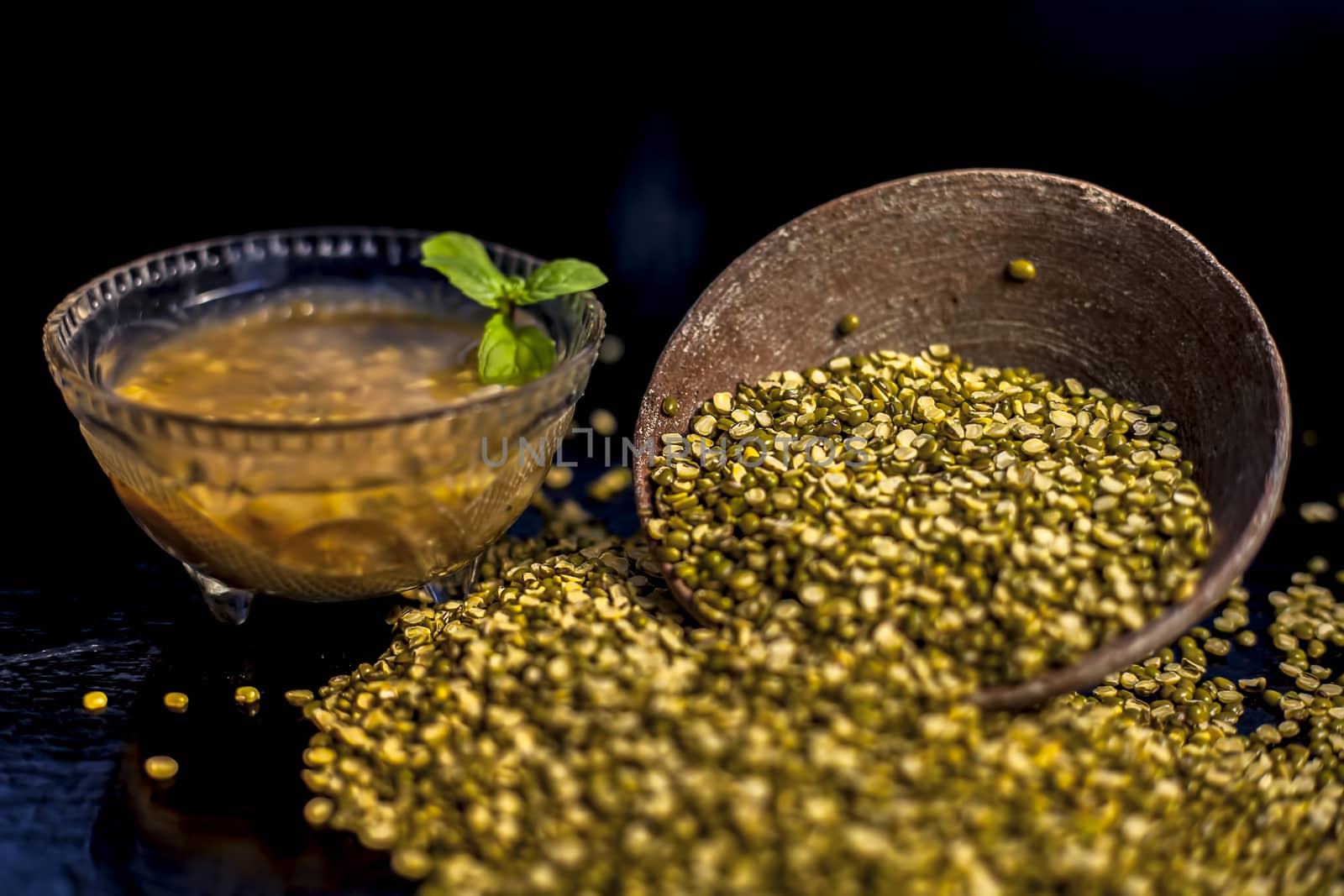 Close shot of mung bean or moong dal in a clay bowl along with some water and moong dal well mixed on a black glossy surface. Horizontal shot with Rembrandt lighting technique. by mirzamlk