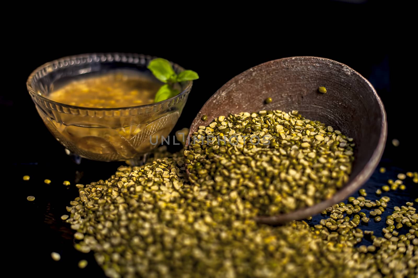 Close shot of mung bean or moong dal in a clay bowl along with some water and moong dal well mixed on a black glossy surface. Horizontal shot with Rembrandt lighting technique. by mirzamlk