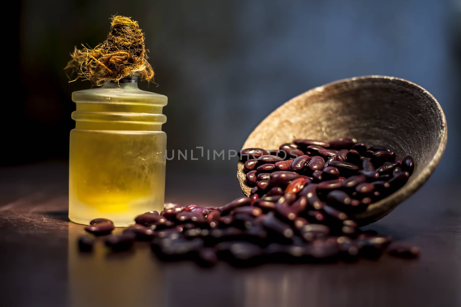 Close up of raw kidney beans on brown colored surface in a clay bowl and its oil in a small transparent glass bottle with a spotlight on it. Horizontal shot. by mirzamlk