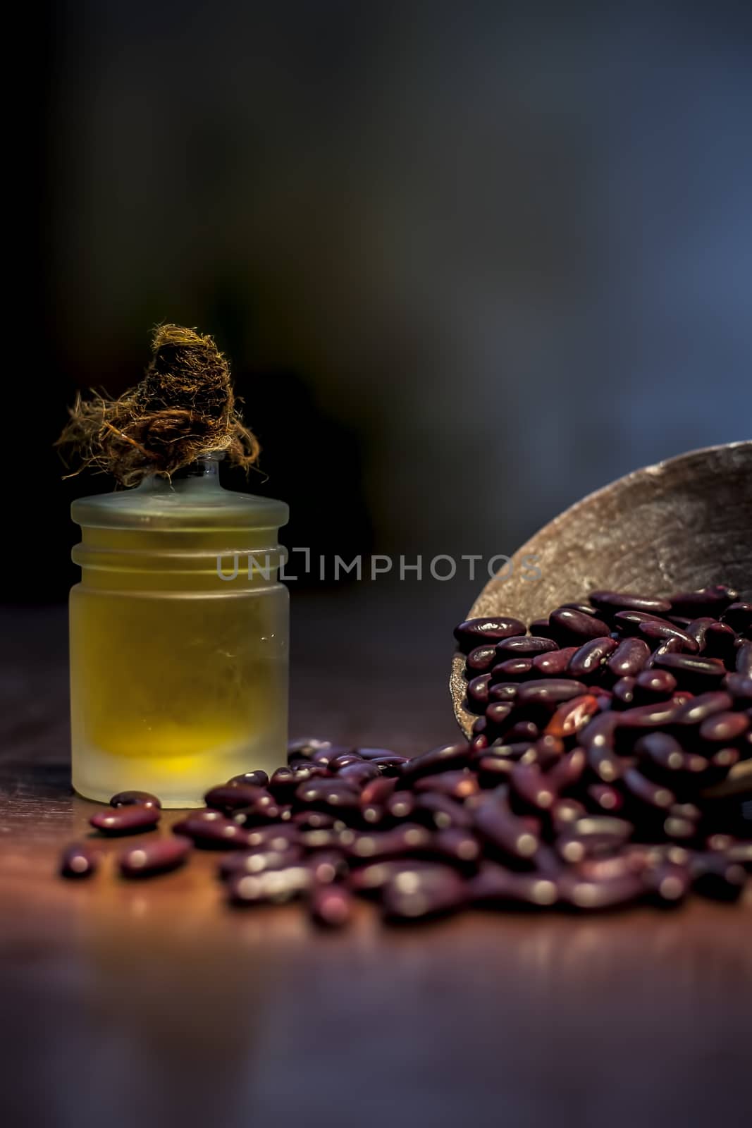 Close up of raw kidney beans on brown colored surface in a clay bowl and its oil in a small transparent glass bottle with a spotlight on it. Vertical shot. by mirzamlk