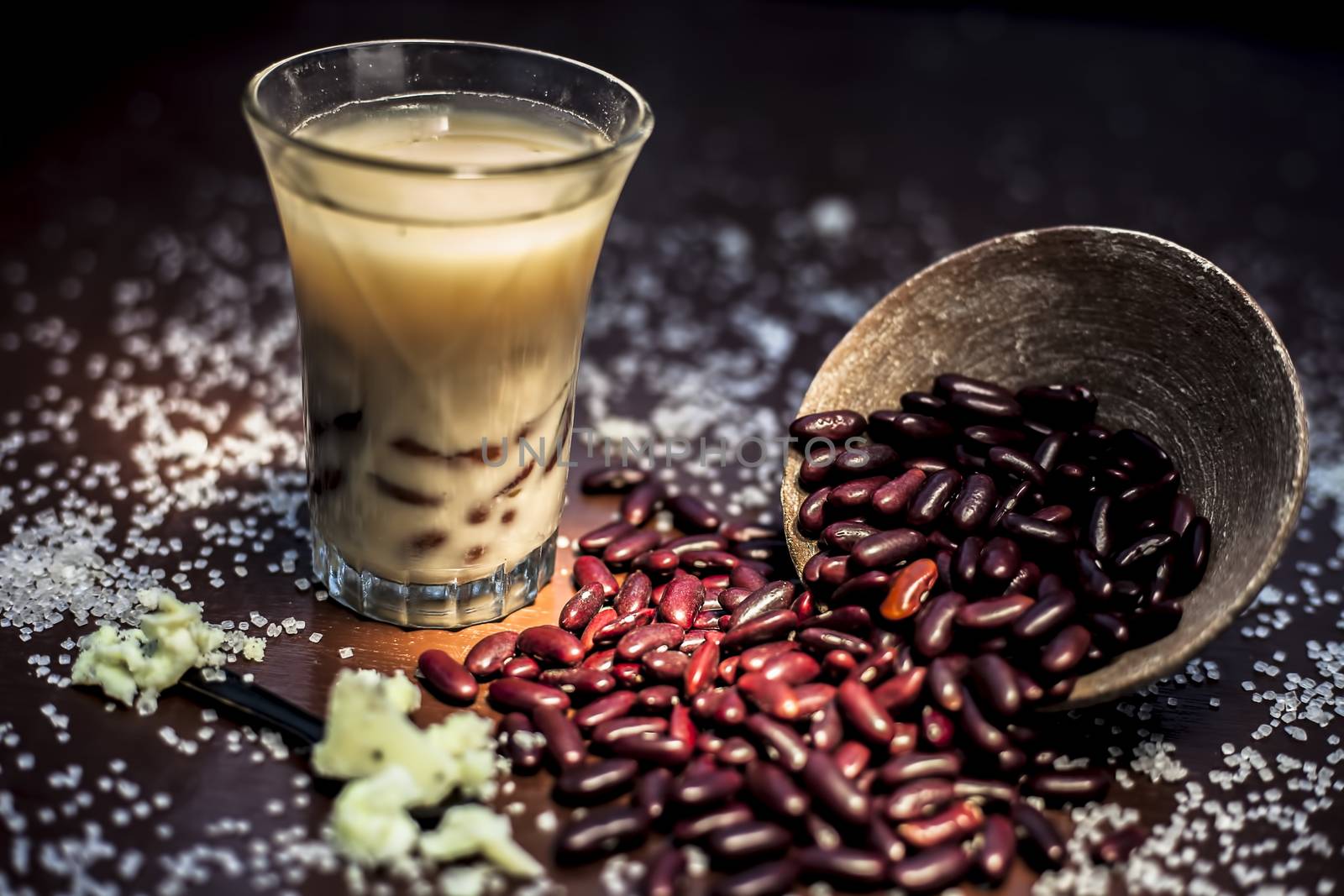 Red bean bubble tea in a glass along with some raw kidney beans, butter and sugar on the brown surface with Rembrandt light technique. Horizontal shot.