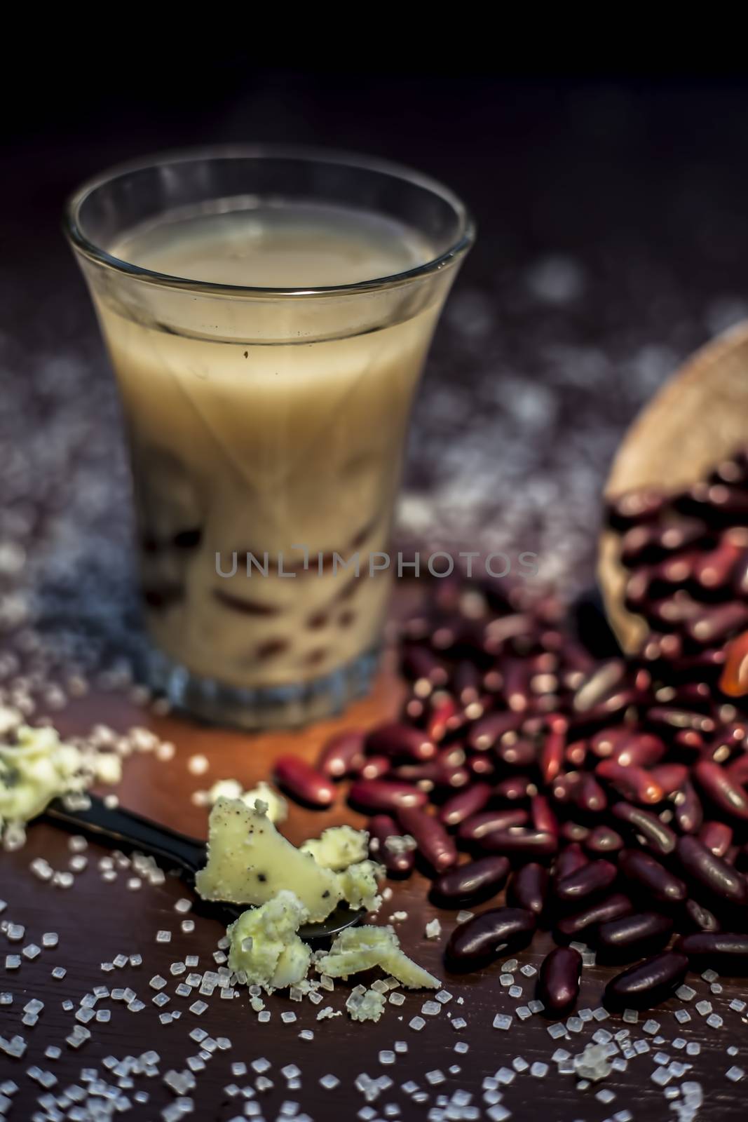 Red bean bubble tea in a glass along with some raw kidney beans, butter and sugar on the brown surface with Rembrandt light technique. Vertical shot.