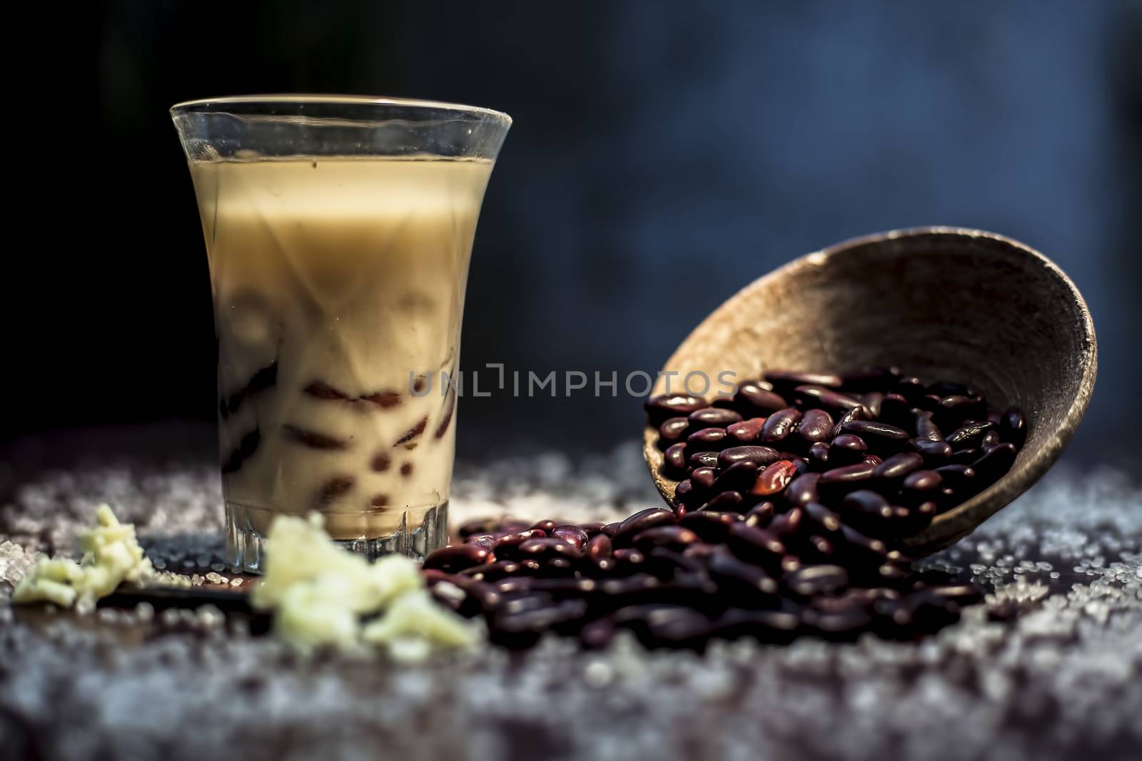 Red bean bubble tea in a glass along with some raw kidney beans, butter and sugar on the brown surface with Rembrandt light technique. Horizontal shot.