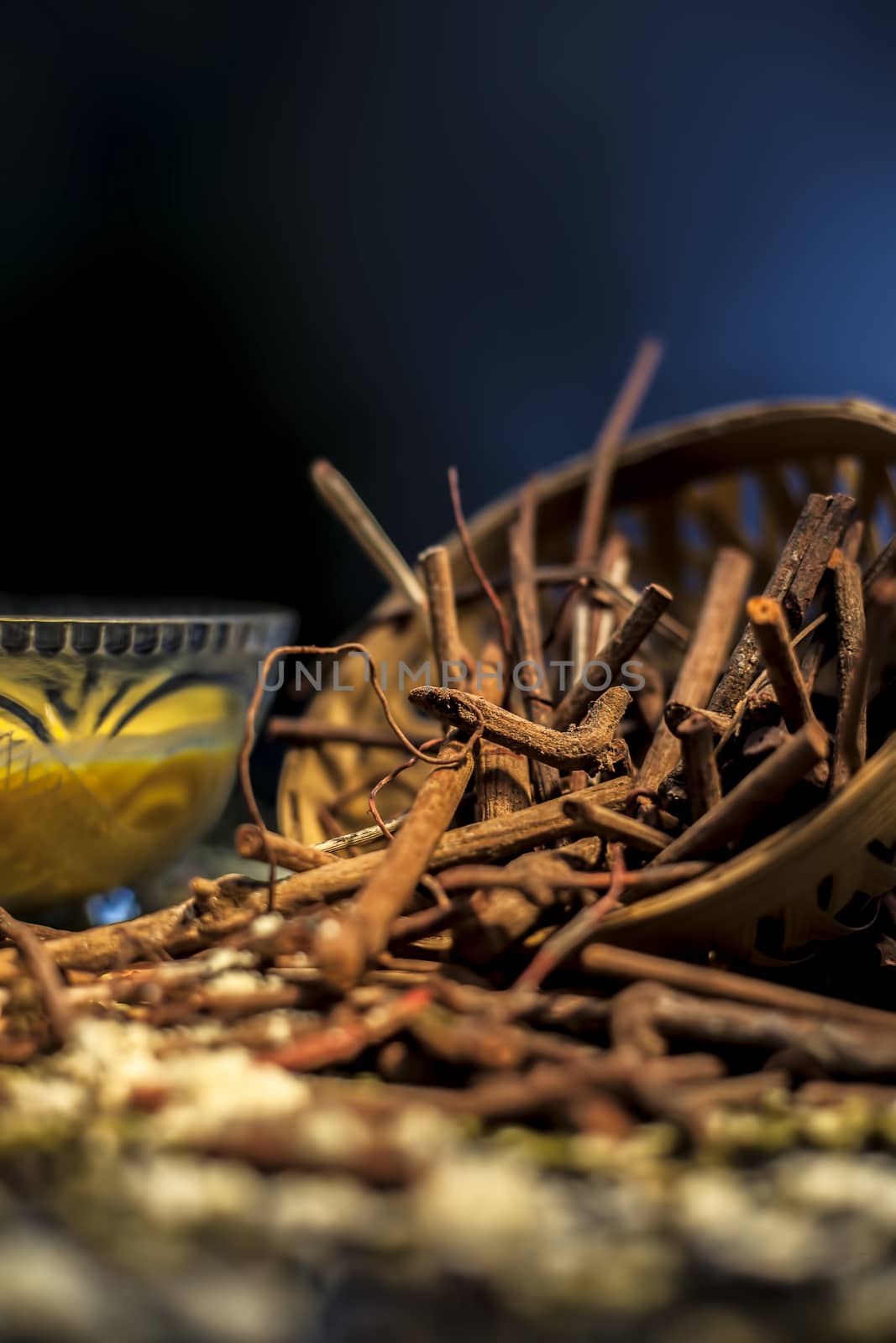 Close up shot of a bunch of manjistha herb roots in a container on a blue surface along with some other ingredients with it.