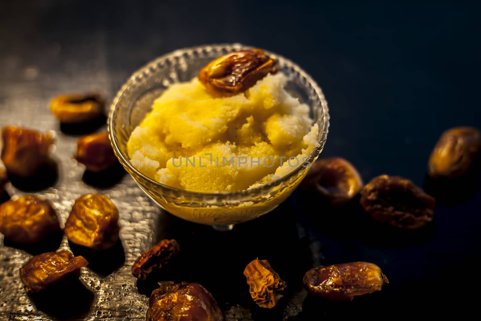 Close up shot of dates soaked in ghee for better stamina and health on black wooden surface along with ghee or clarified butter. Horizontal shot.