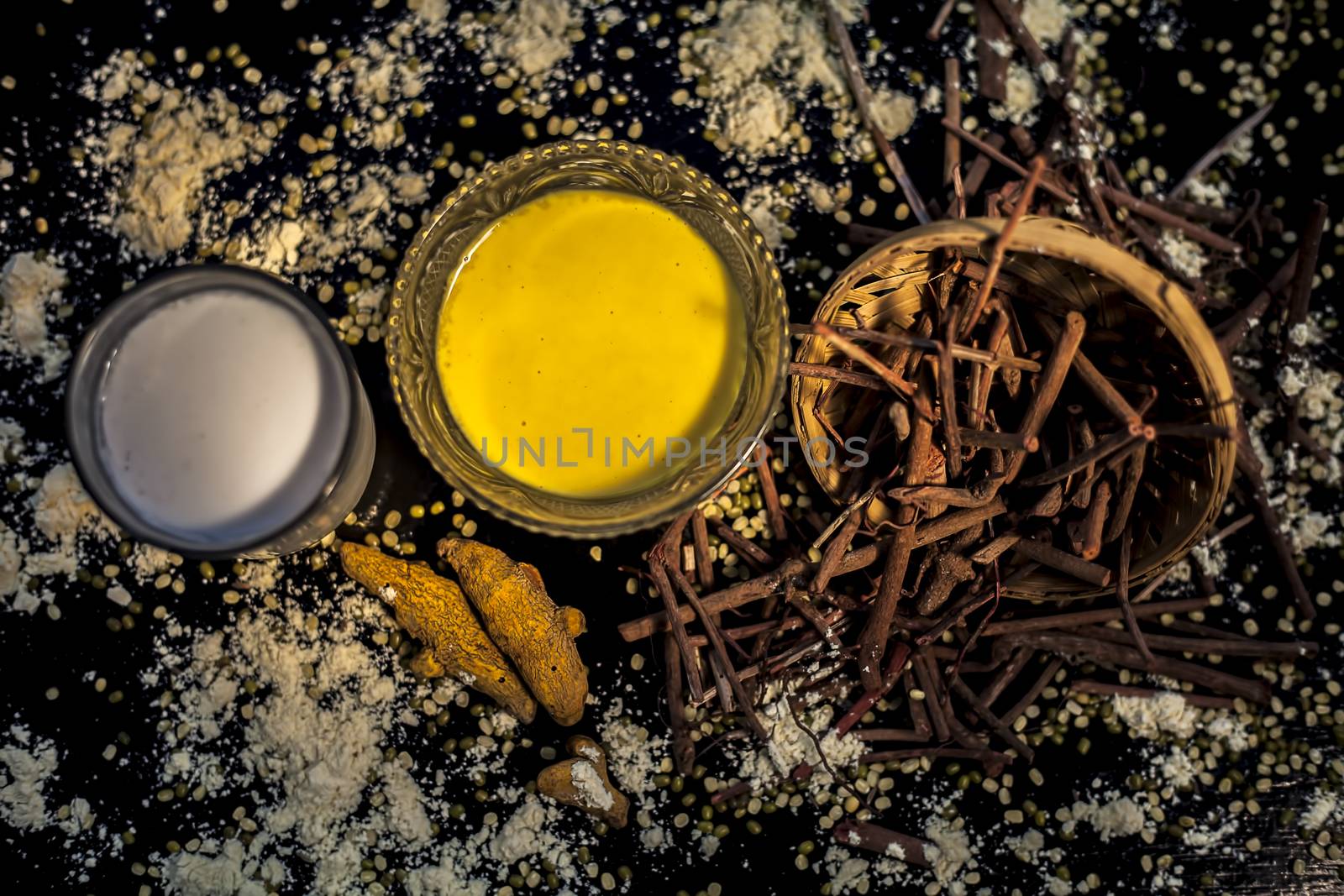Ayurvedic blood purifier and skin glow face mask consisting of Manjistha, mung bean, haldi/turmeric, and milk. Horizontal shot of face mask with entire constituents with it on a black surface.