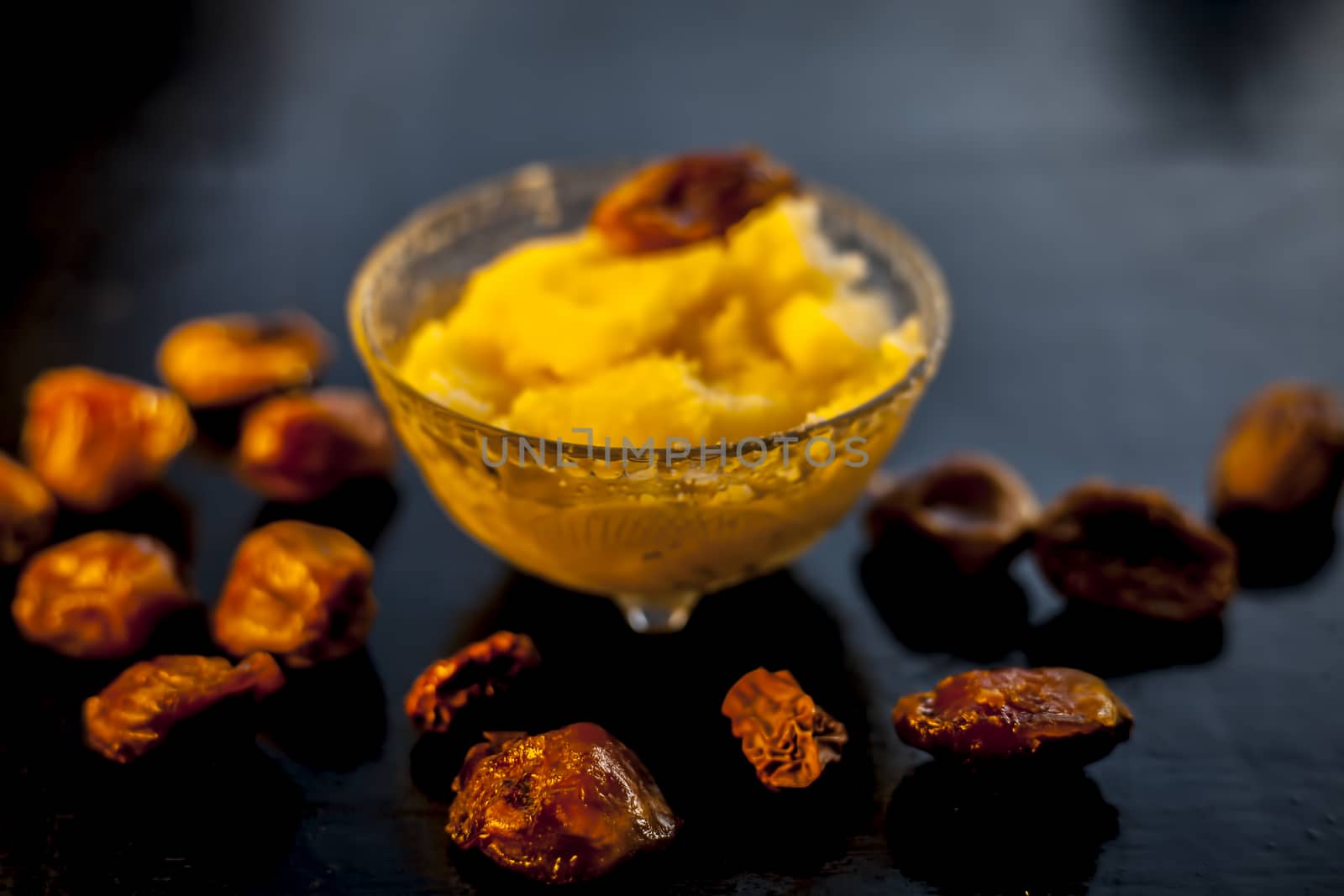 Close up shot of dates soaked in ghee for better stamina and health on black wooden surface along with ghee or clarified butter. Horizontal shot. by mirzamlk