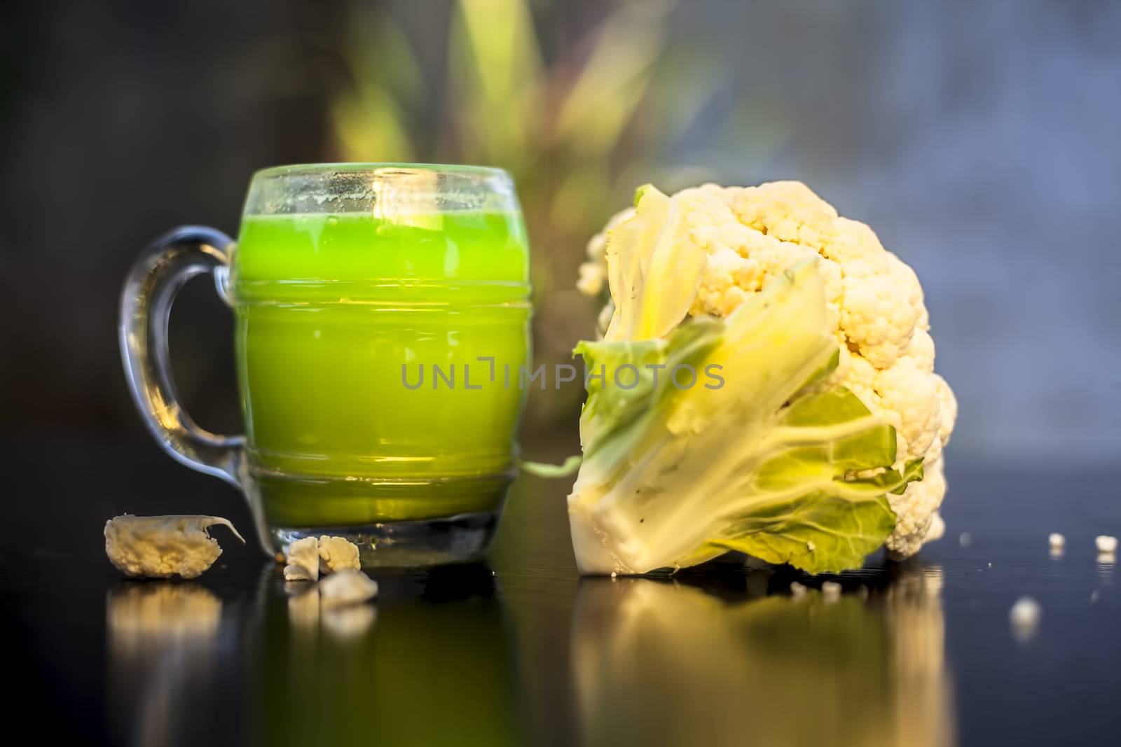 Close up shot of raw cauliflower and its healthy juice in a glass on a black surface with selective focus, creative lighting, and blurred background.