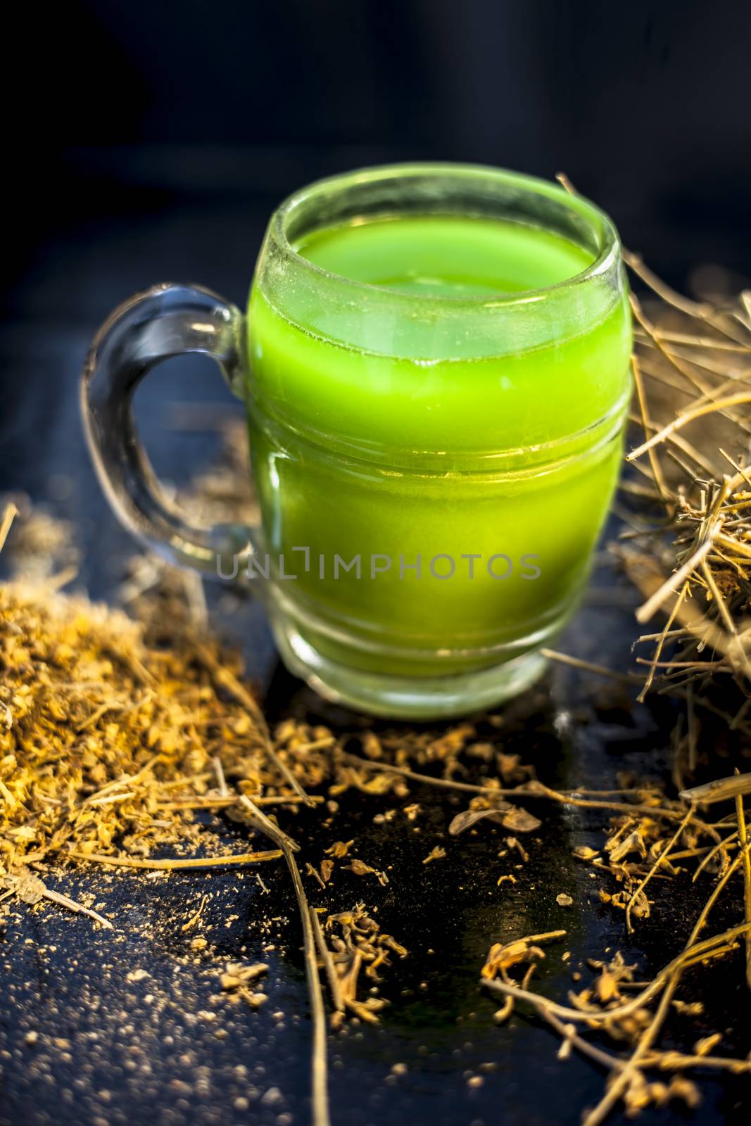 ayurvedic memory booster herb shankhpushpi or Convolvulus pluricaulis roots along with its extract herbal juice in a glass on a black wooden surface with selective focus and blurred background.