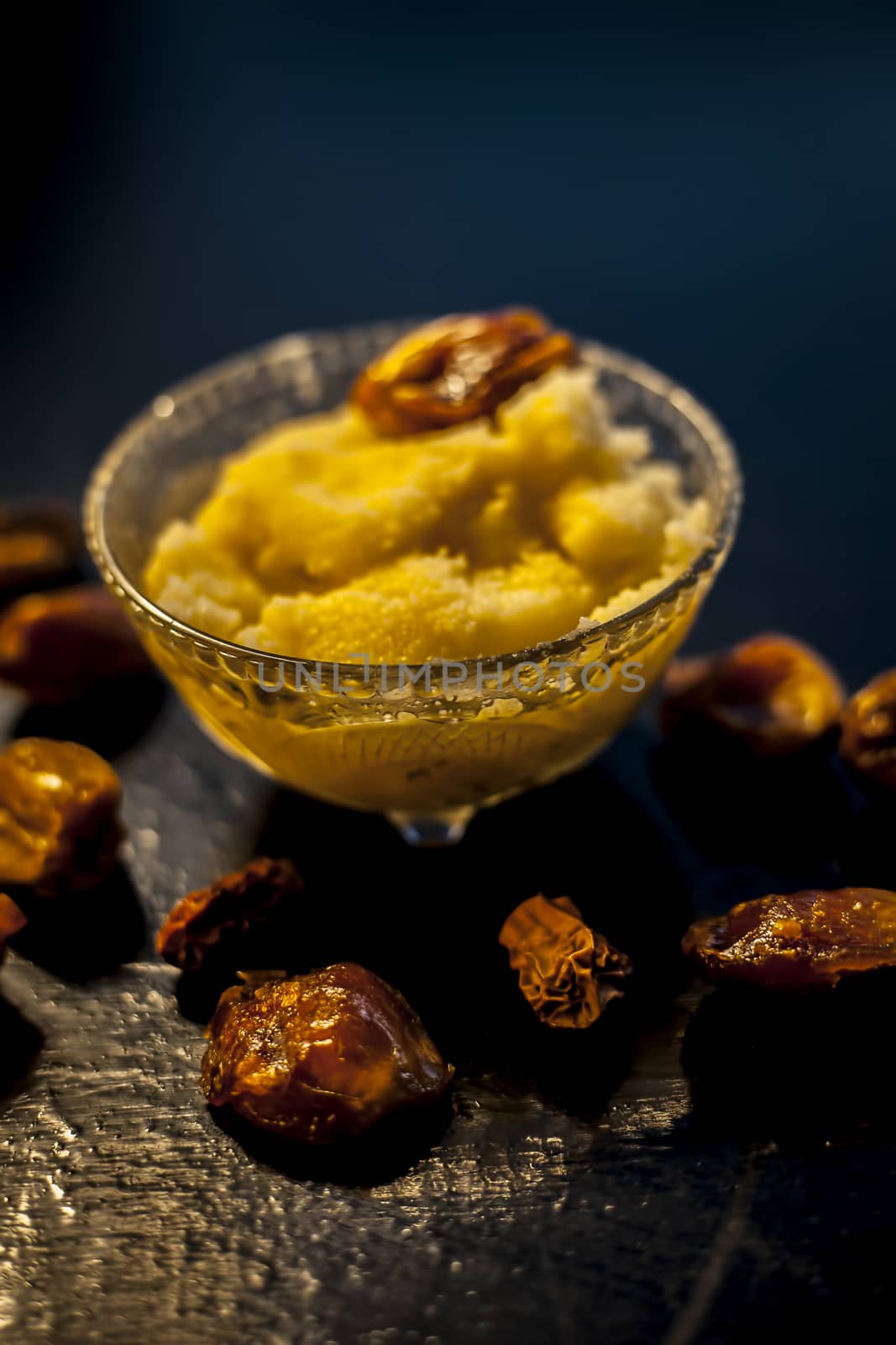 Close up shot of dates soaked in ghee for better stamina and health on black wooden surface along with ghee or clarified butter. Vertical shot.