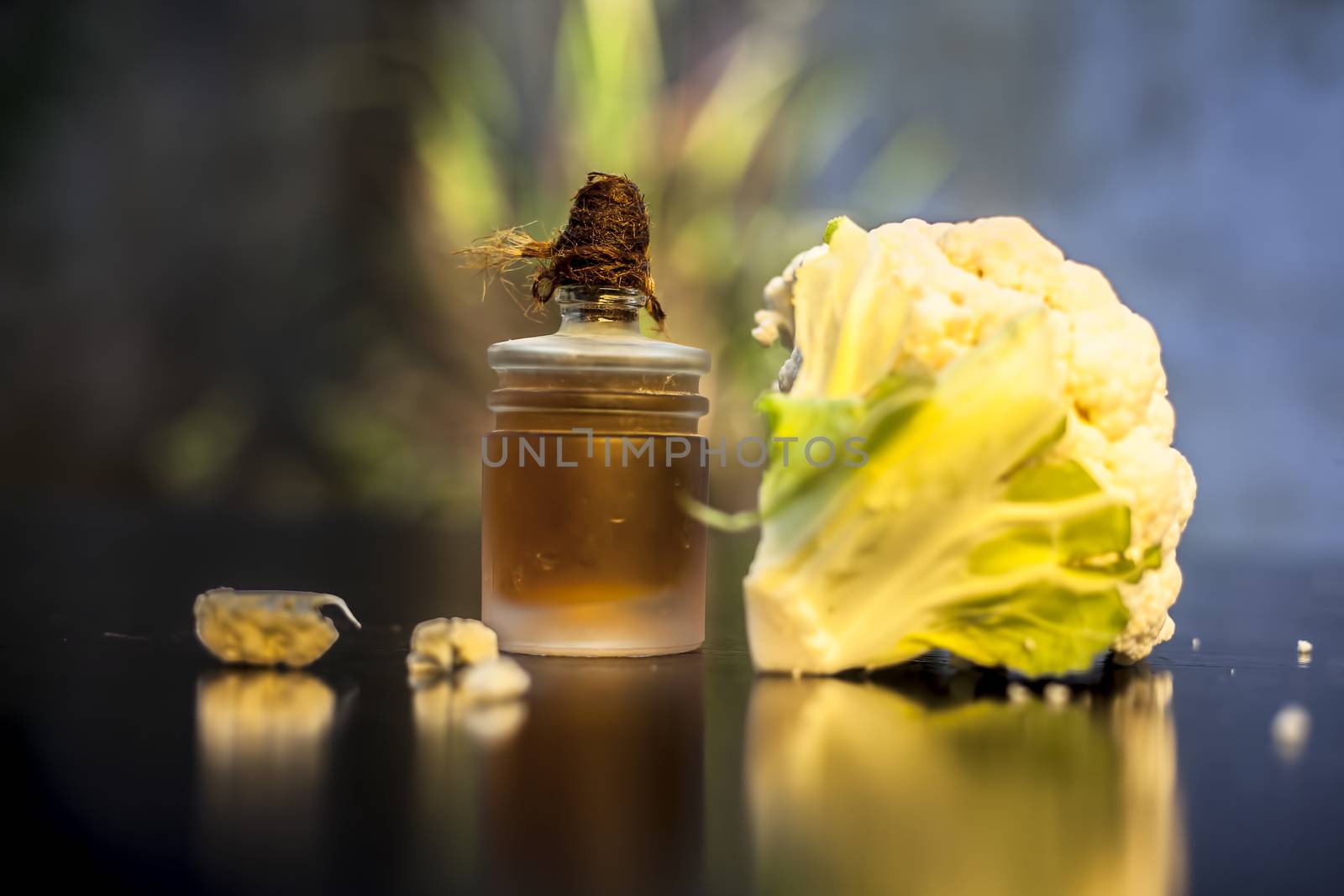 Close up shot of raw cauliflower and its essential oil in a small glass bottle on a black surface with selective focus, creative lighting, and blurred background.