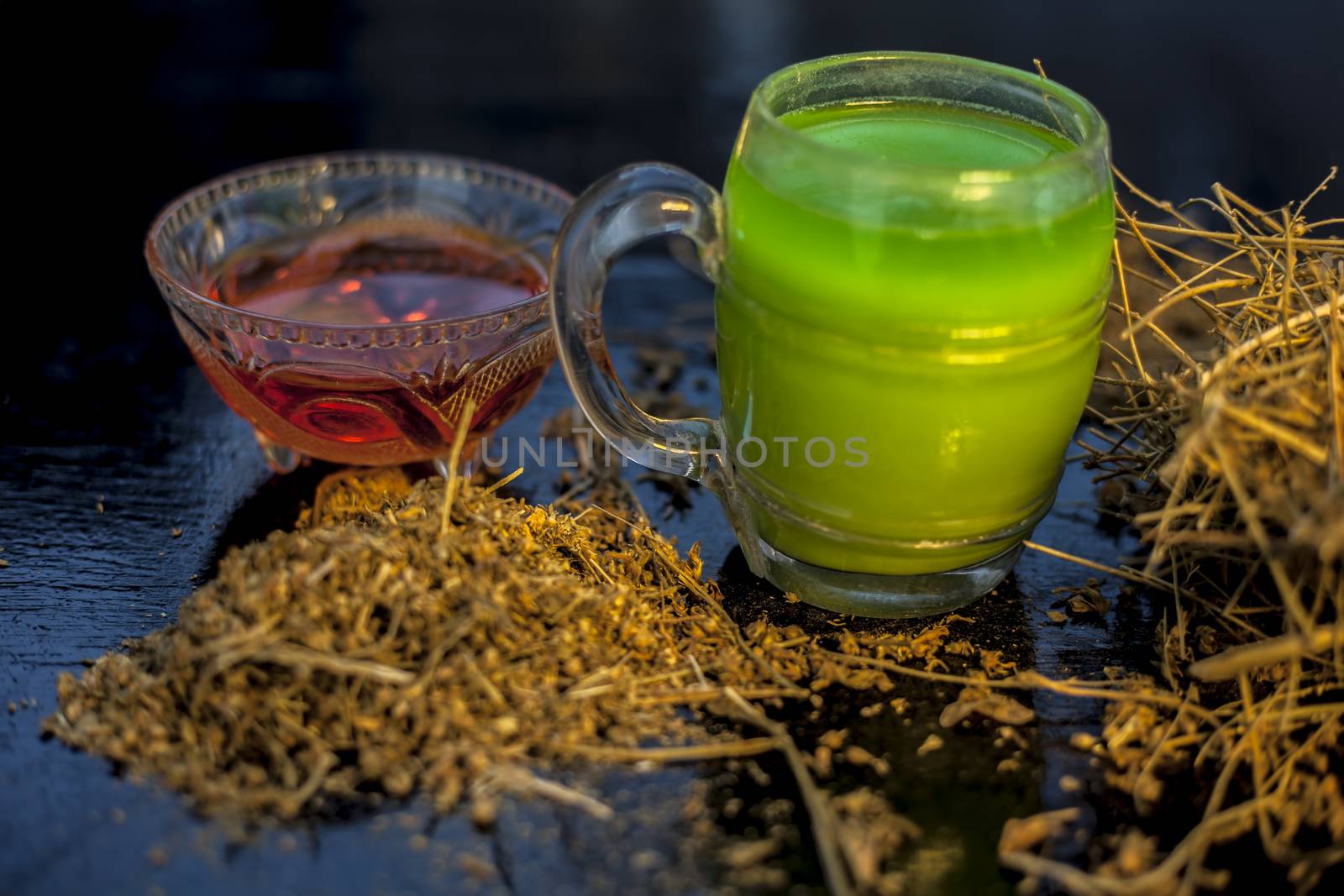 Close up of green-colored extracted juice shankhpushpi or Convolvulus pluricaulis roots along with its extract herbal juice in a glass on a black wooden surface.