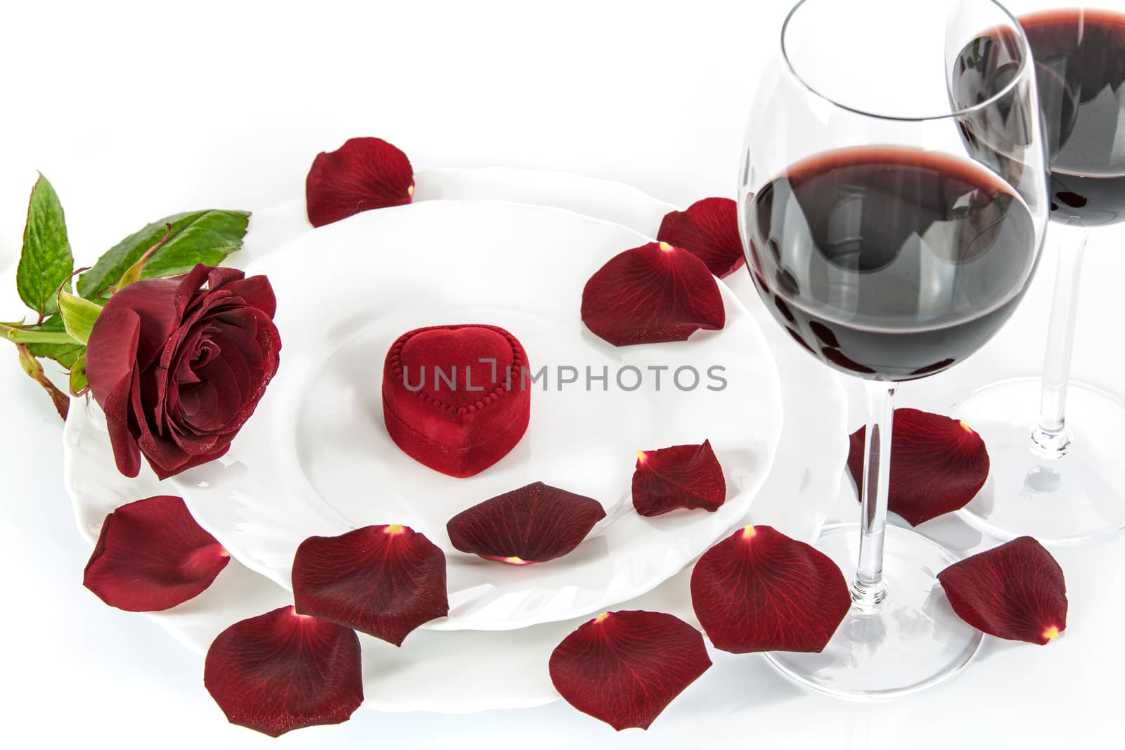 Table setting for a romantic Valentines Day dinner with a red rose, red wine and gift.