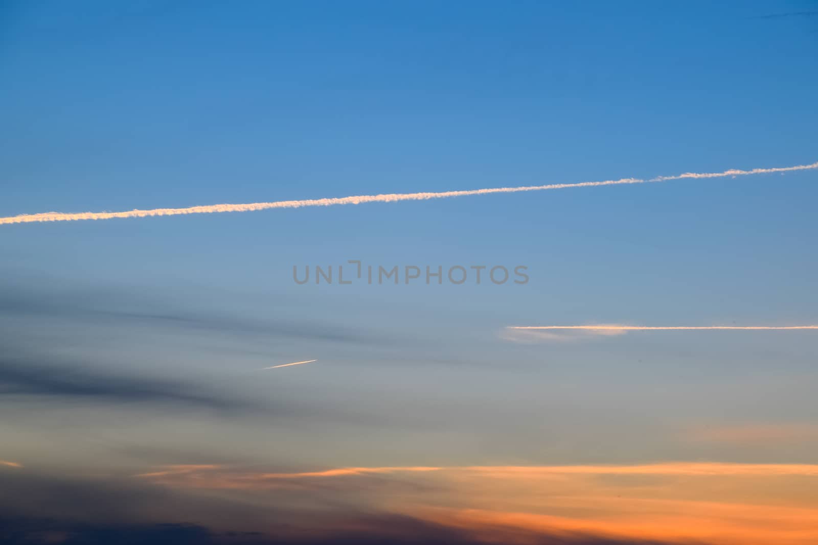 Contrail from an airplane on a blue sky against a sunset.