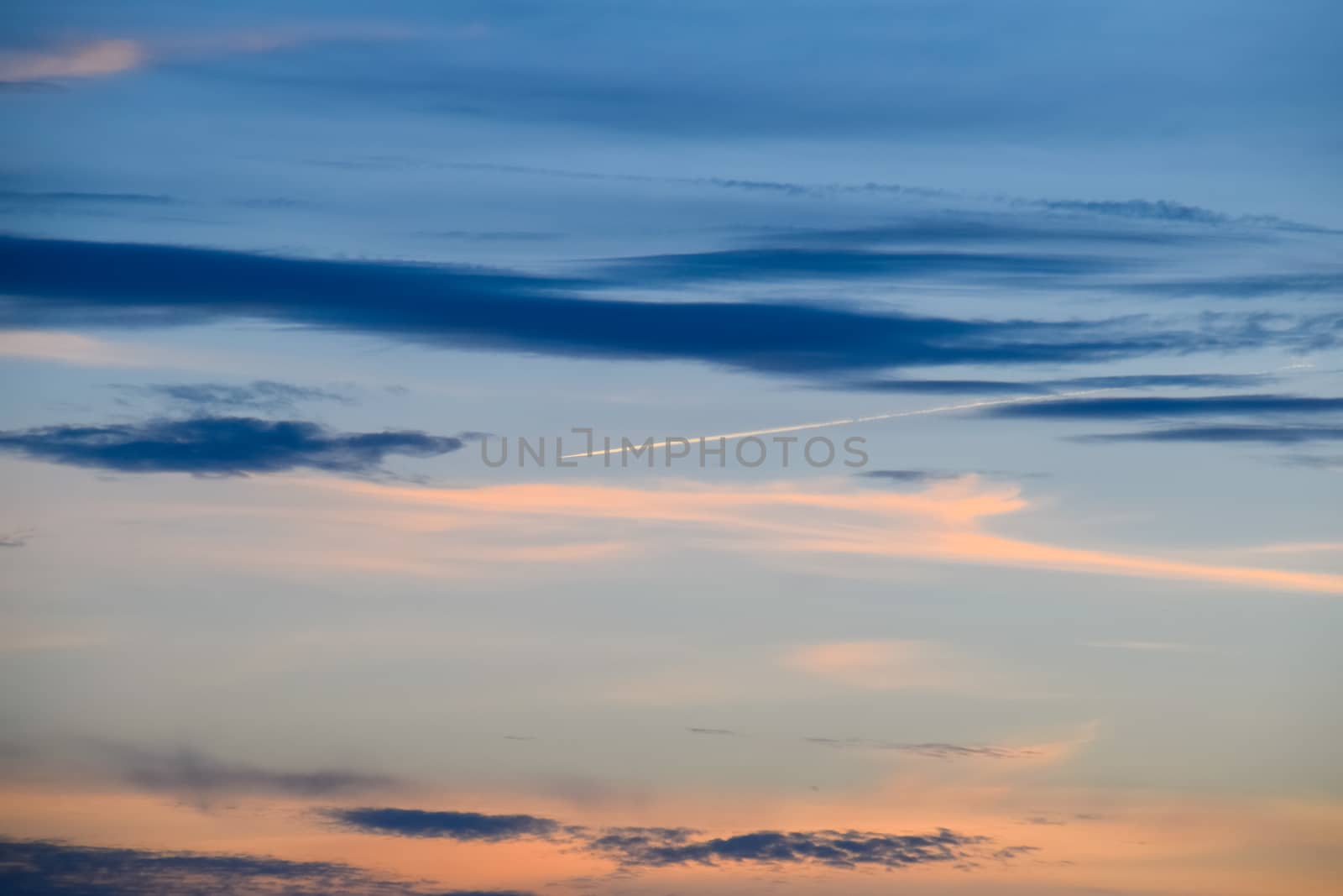 Contrail from an airplane on a blue sky against a sunset.