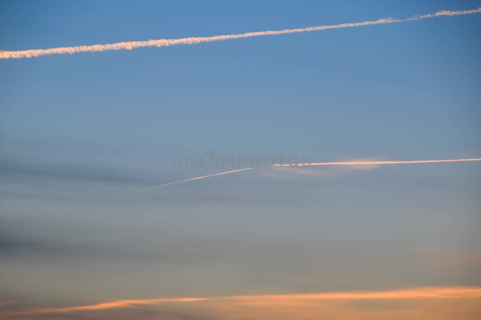 Contrail from an airplane on a blue sky against a sunset.